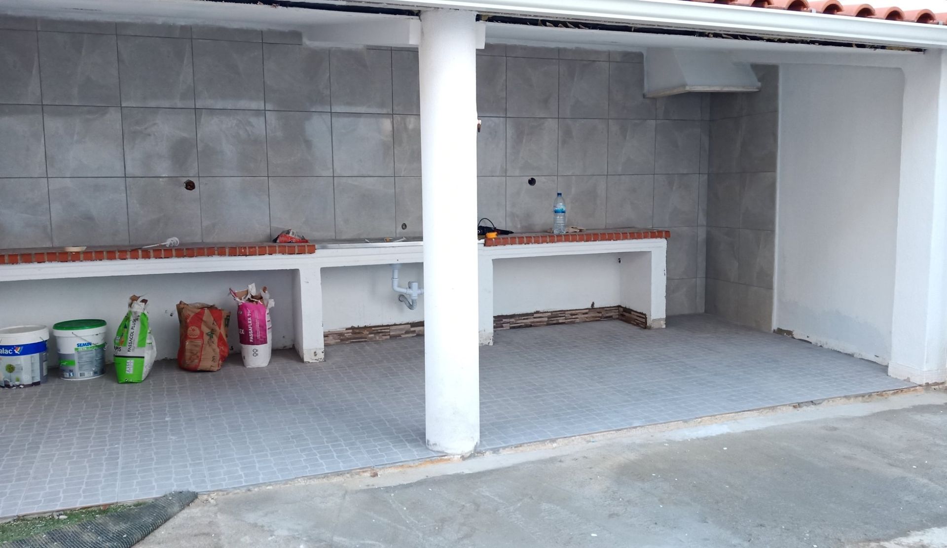 Área externa coberta com bancadas de azulejo, detalhes em tijolo e um pilar central.