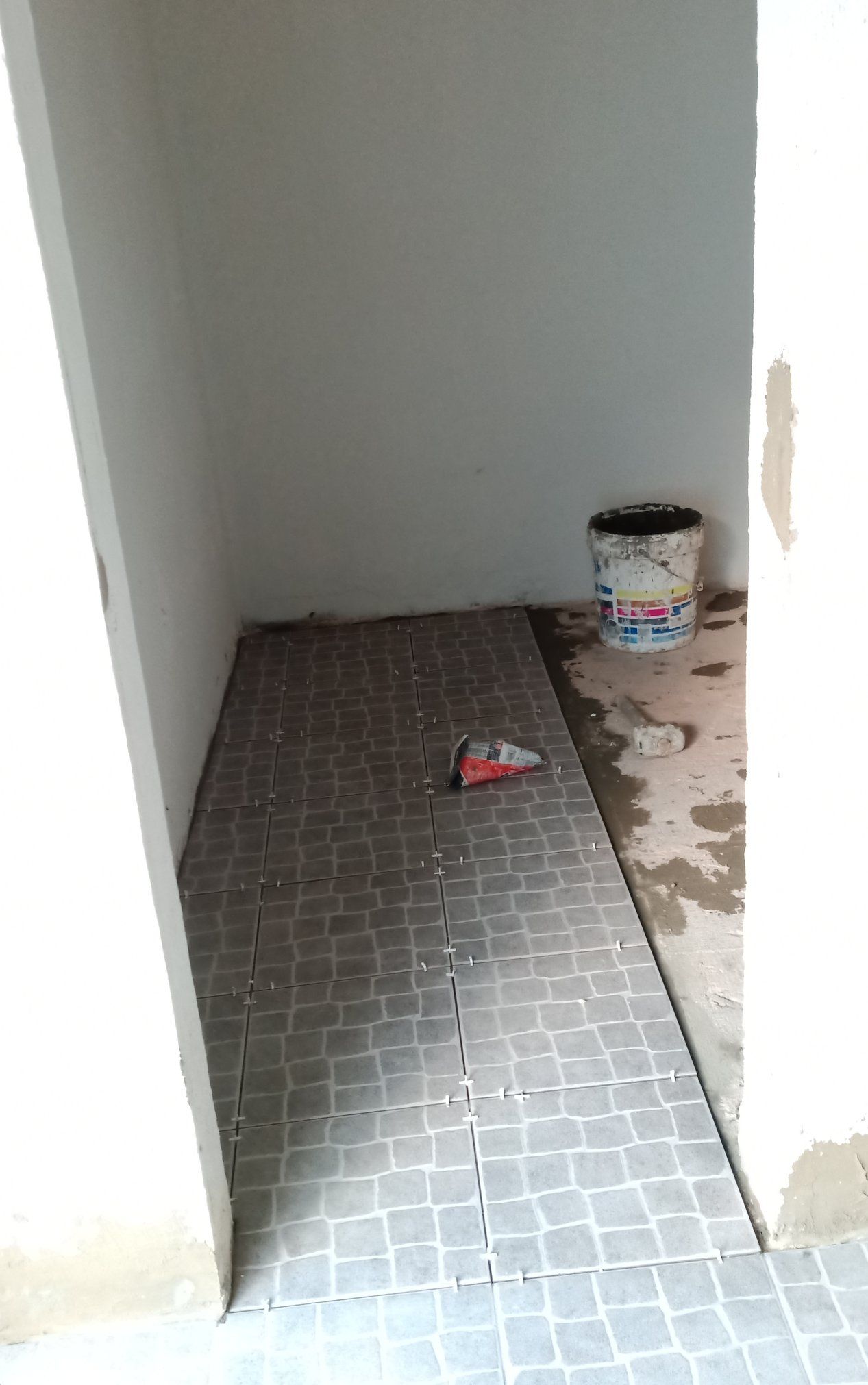 Porta estreita com piso parcialmente revestido de azulejos. Um balde de tinta está no canto.