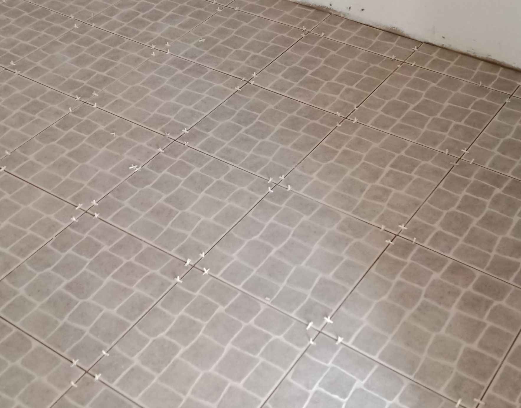 Piso de azulejos cinza com espaçadores brancos entre os azulejos.