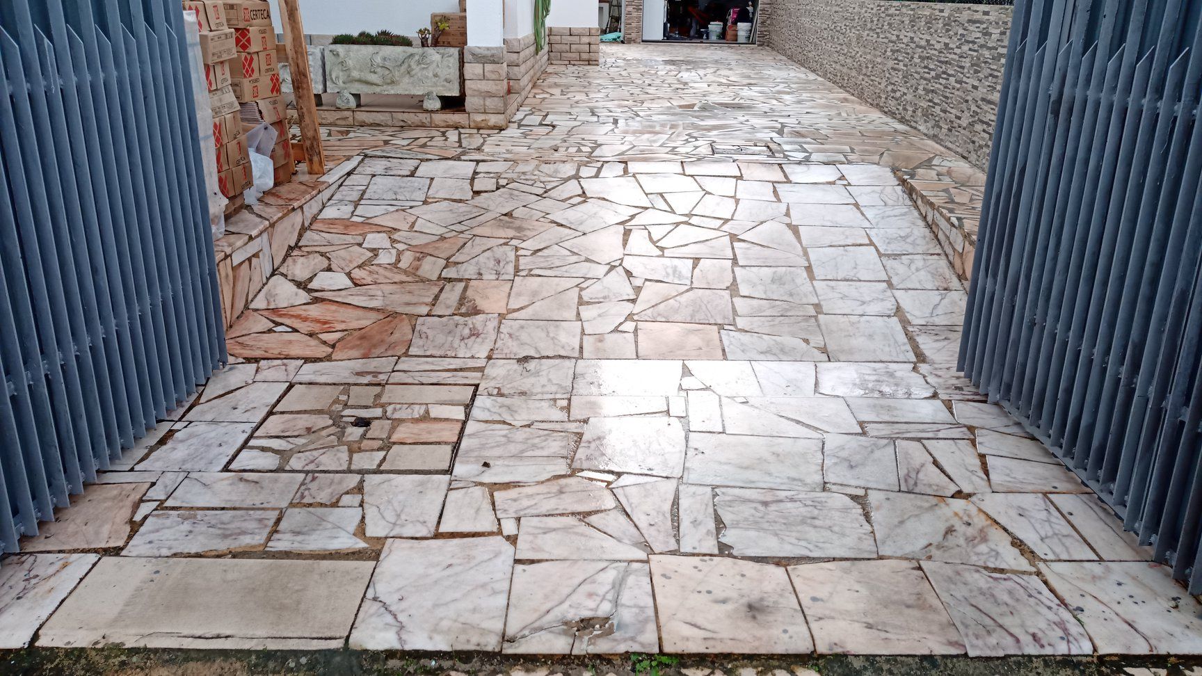 Passarela de pedra que leva a uma área cercada, com ladrilhos claros de formato irregular.