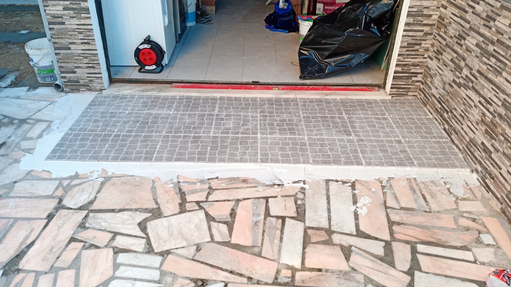 Entrada com uma plataforma de concreto texturizado, delimitando um caminho de lajes de pedra. Uma porta está ao fundo.