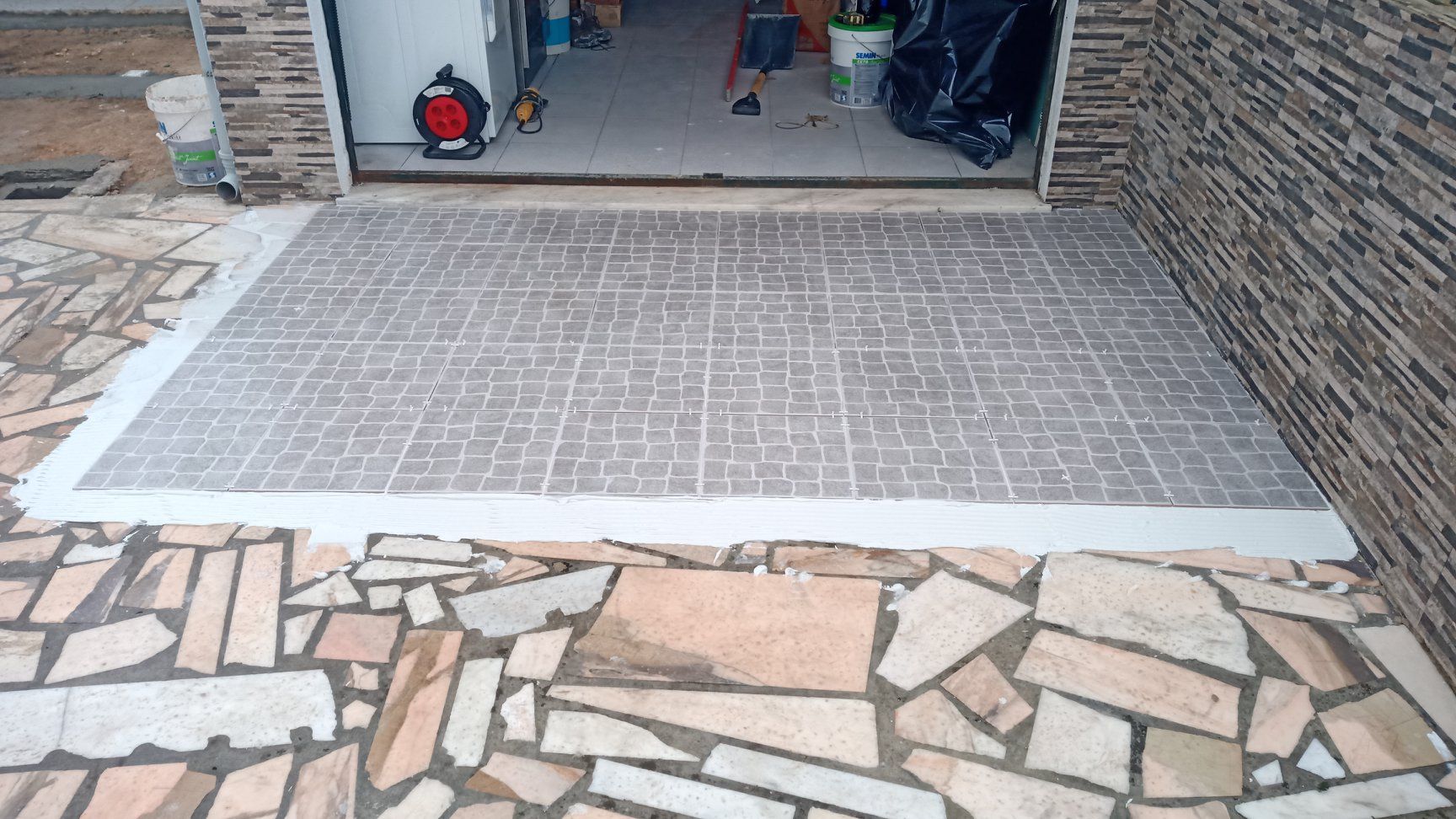 Entrada de veículos em concreto com textura em tons de cinza e branco, delimitada por caminho de pedra, que leva à garagem.