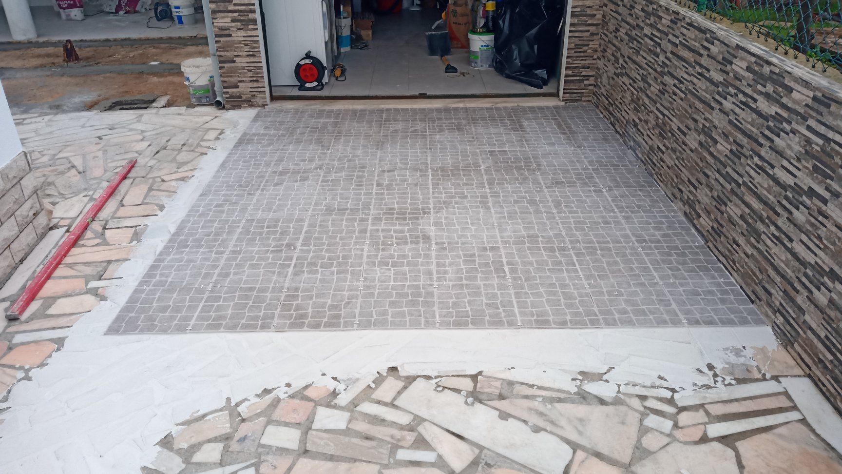 Entrada de automóveis em concreto com desenho padronizado, que leva à garagem. Calçada de pedra em ambos os lados.