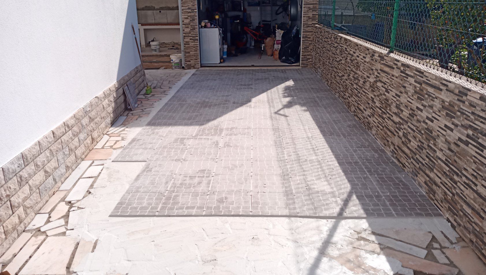 Entrada de automóveis com pavimentação em pedra que leva à garagem. Muros de pedra delimitam as laterais.