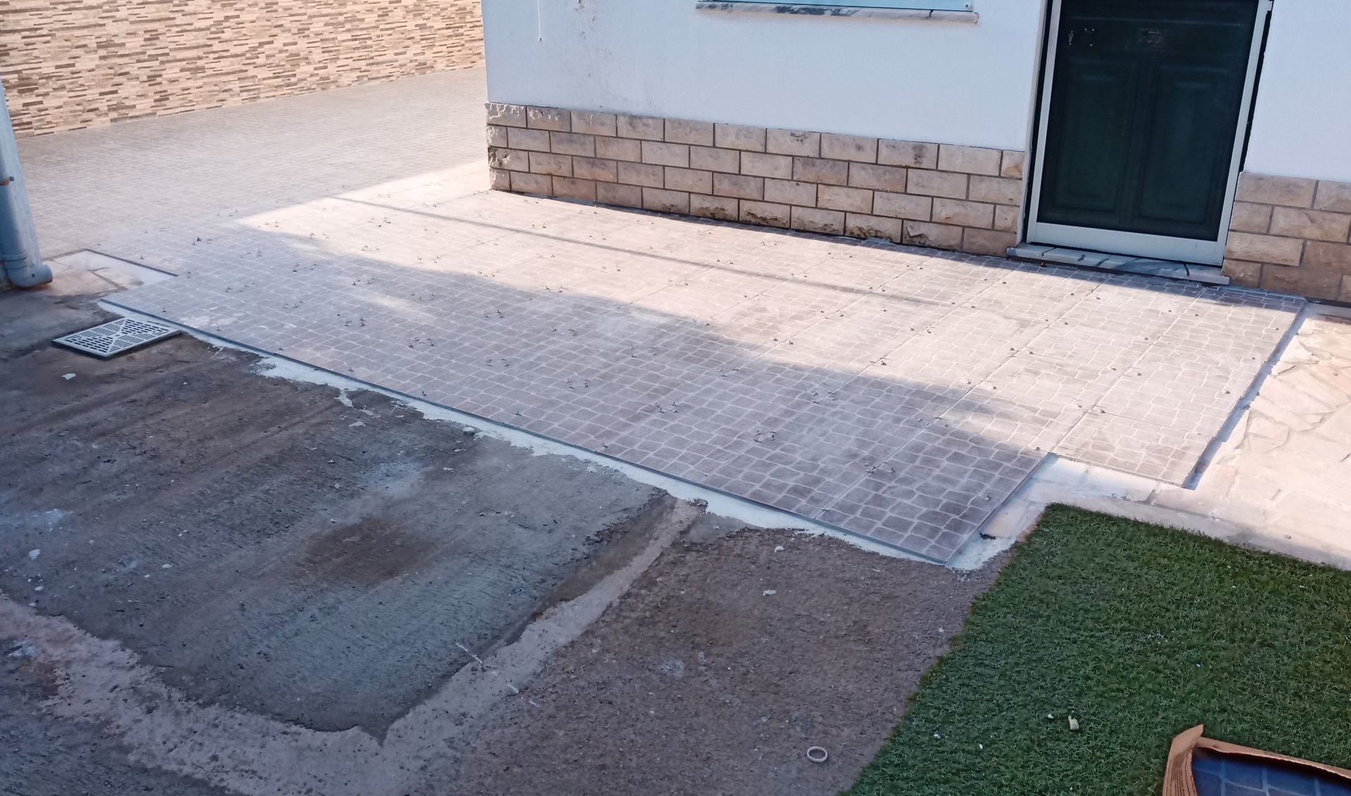 Rampa de concreto que dá acesso à entrada do prédio; uma calçada e um gramado verde também são visíveis.