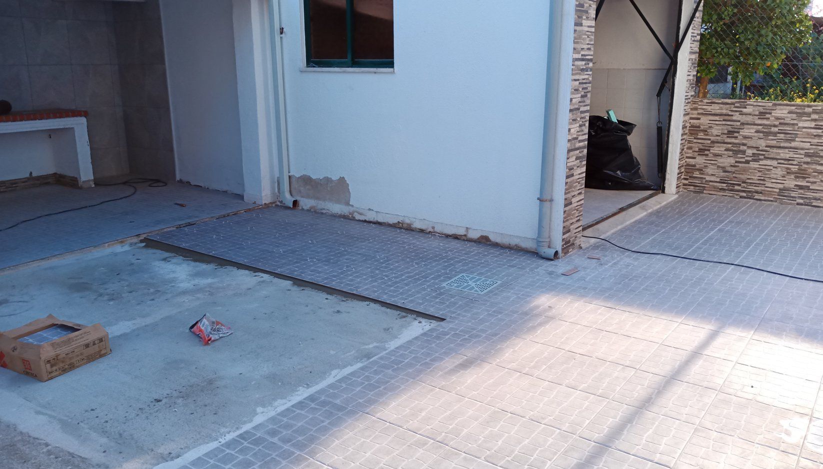 Pátio com base de concreto, pavimentação cinza e acesso a um edifício.