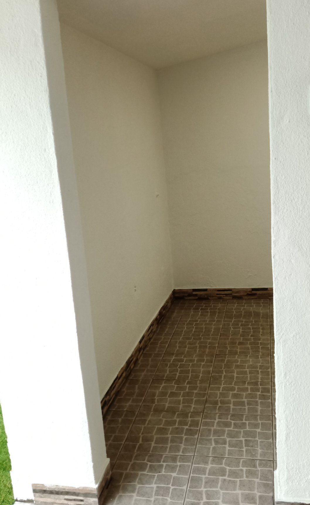 Alcova retangular fechada com paredes bege, piso de azulejo marrom e vigas de sustentação externas brancas.