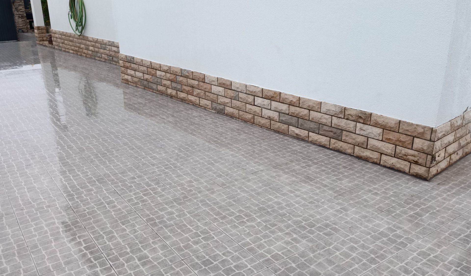 Pátio molhado, revestido com azulejos e com detalhes que imitam tijolos em uma parede branca.