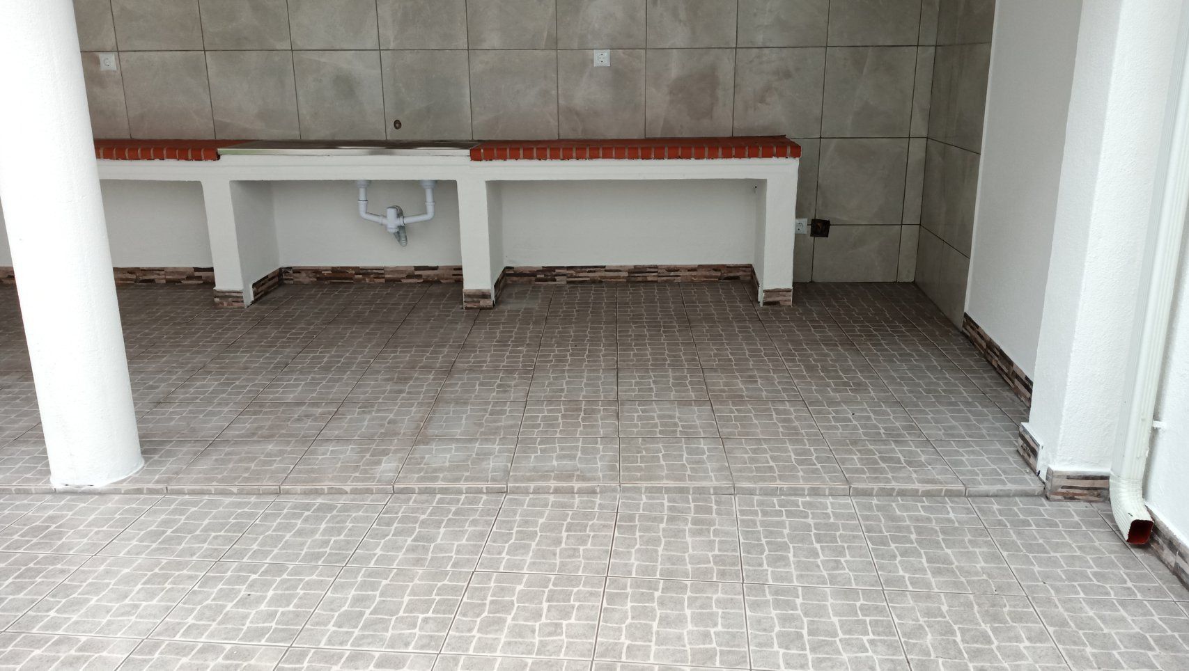 Cozinha externa revestida com azulejos, com bancada, pia e coluna à esquerda.