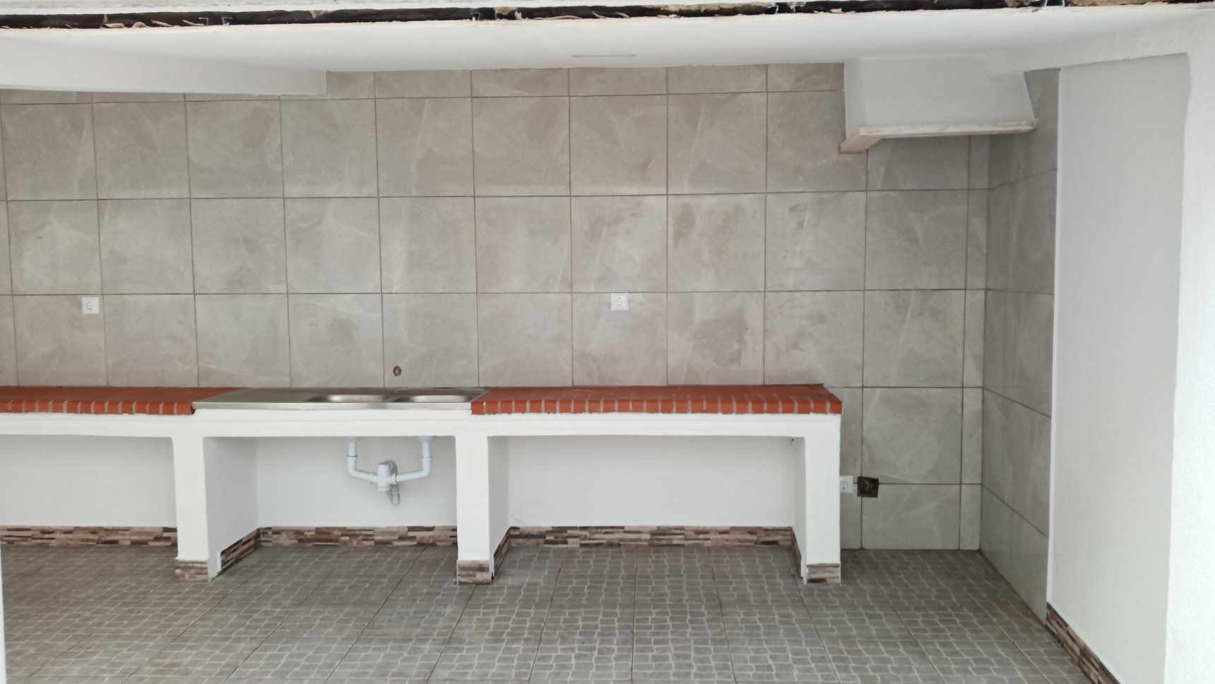 Cozinha externa com backsplash de azulejos e bancadas de tijolos.