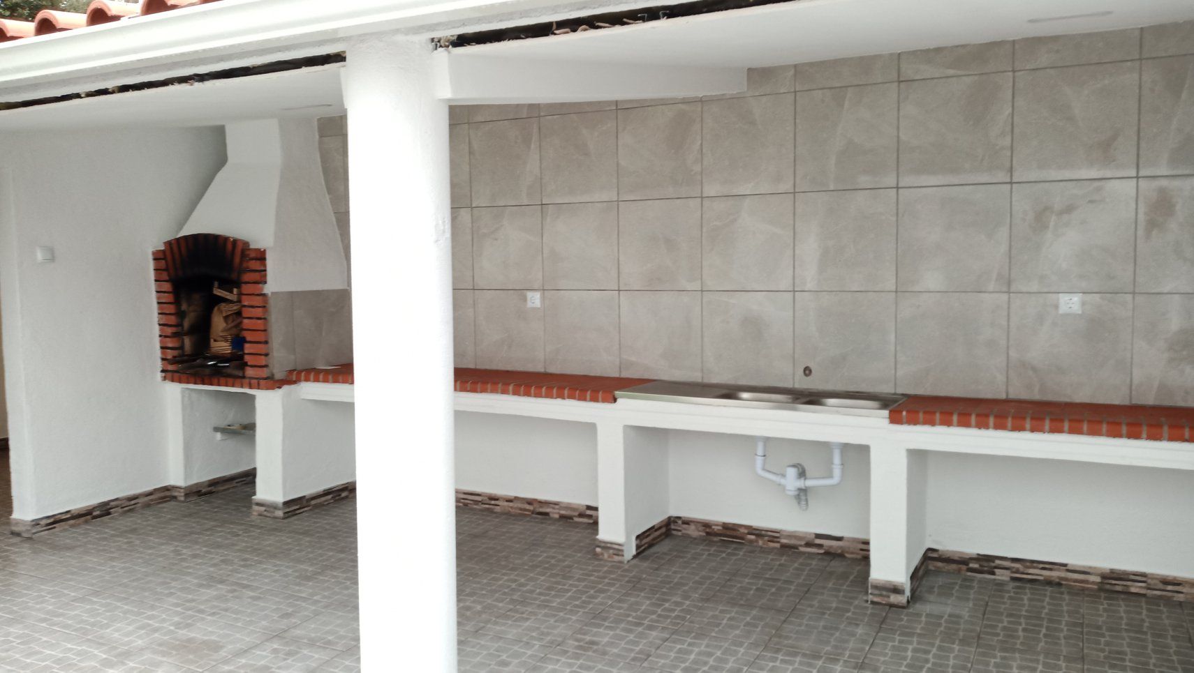 Cozinha externa coberta com churrasqueira de tijolos e bancadas de azulejo.