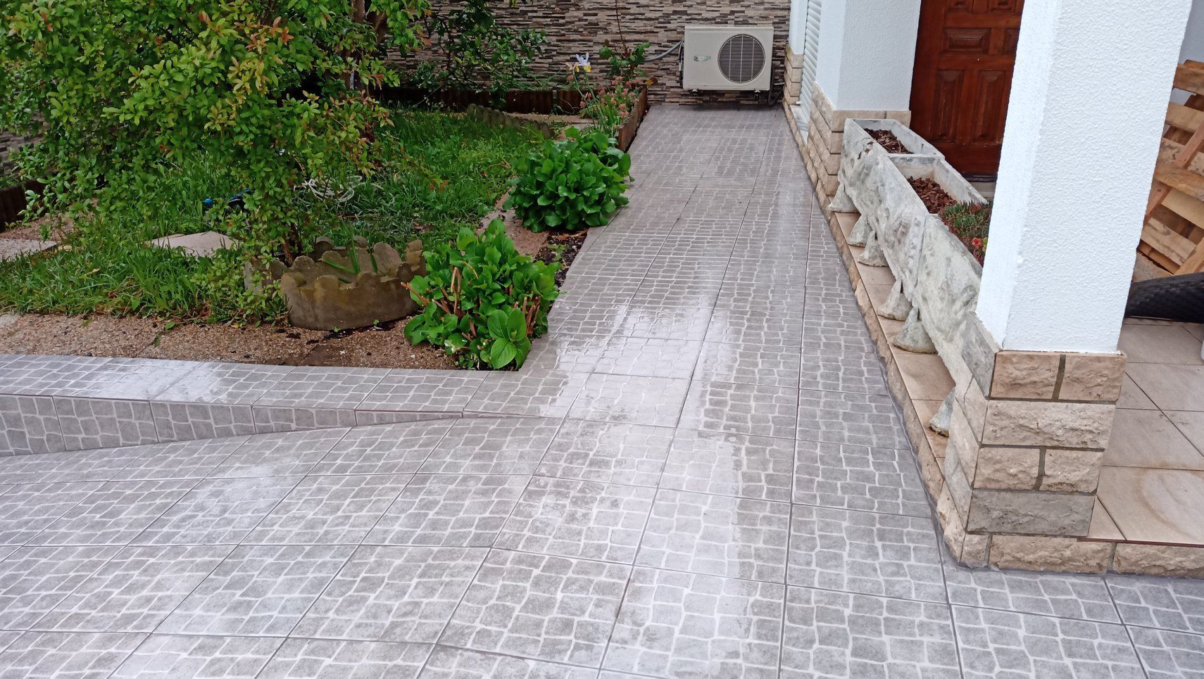 Uma passarela pavimentada ao lado de um jardim e um edifício com uma coluna branca.