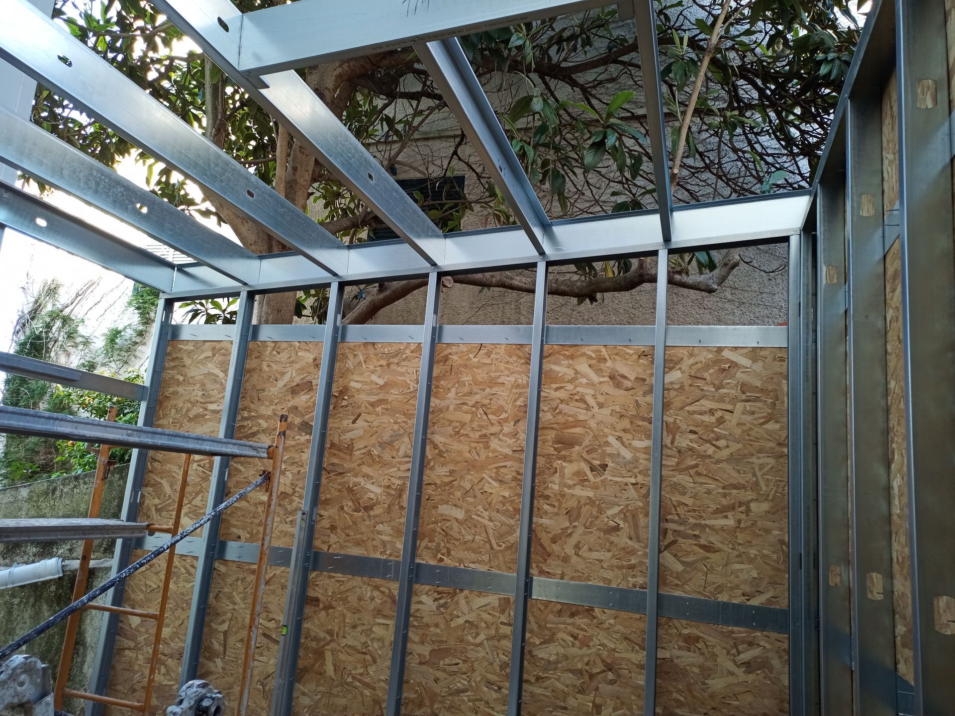 Estrutura metálica com revestimento em OSB, parcialmente construída, em ambiente externo.