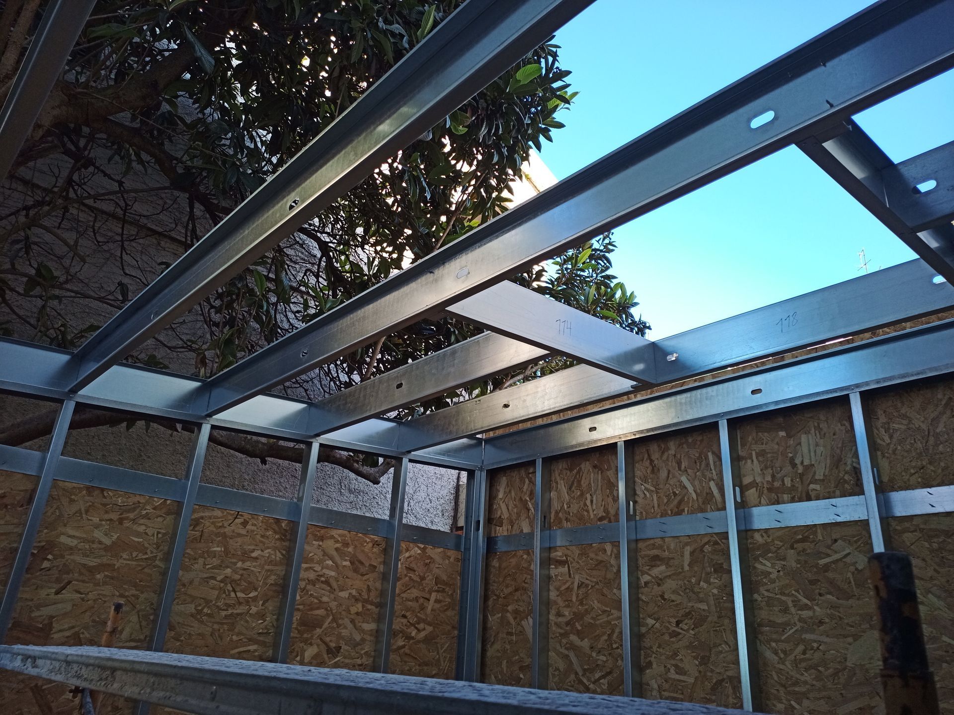 Estrutura metálica com painéis de madeira aparentes. Céu visível através da estrutura do telhado.