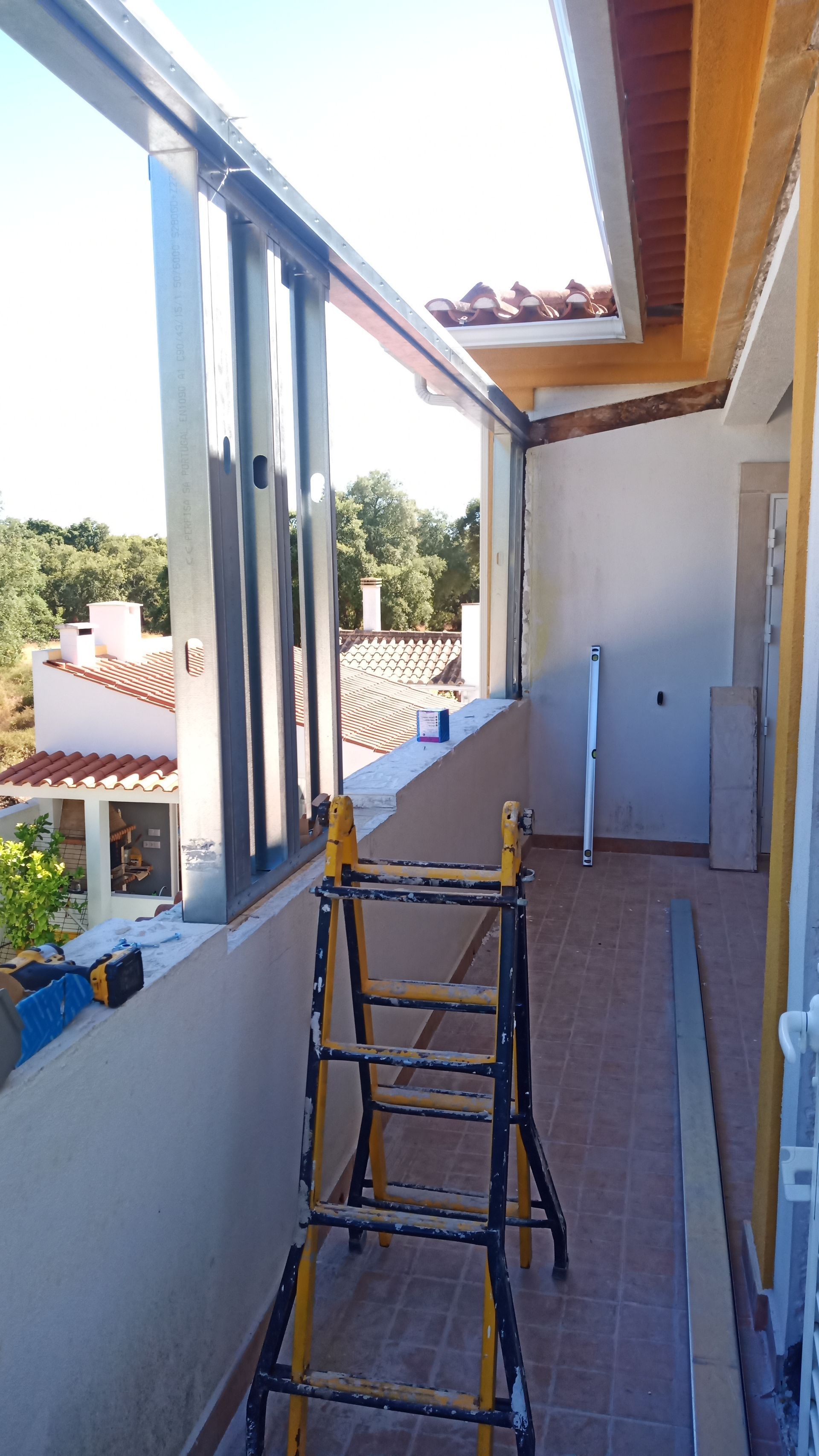 Uma varanda com escada. Guarda-corpo e teto transparentes. Dia ensolarado.
