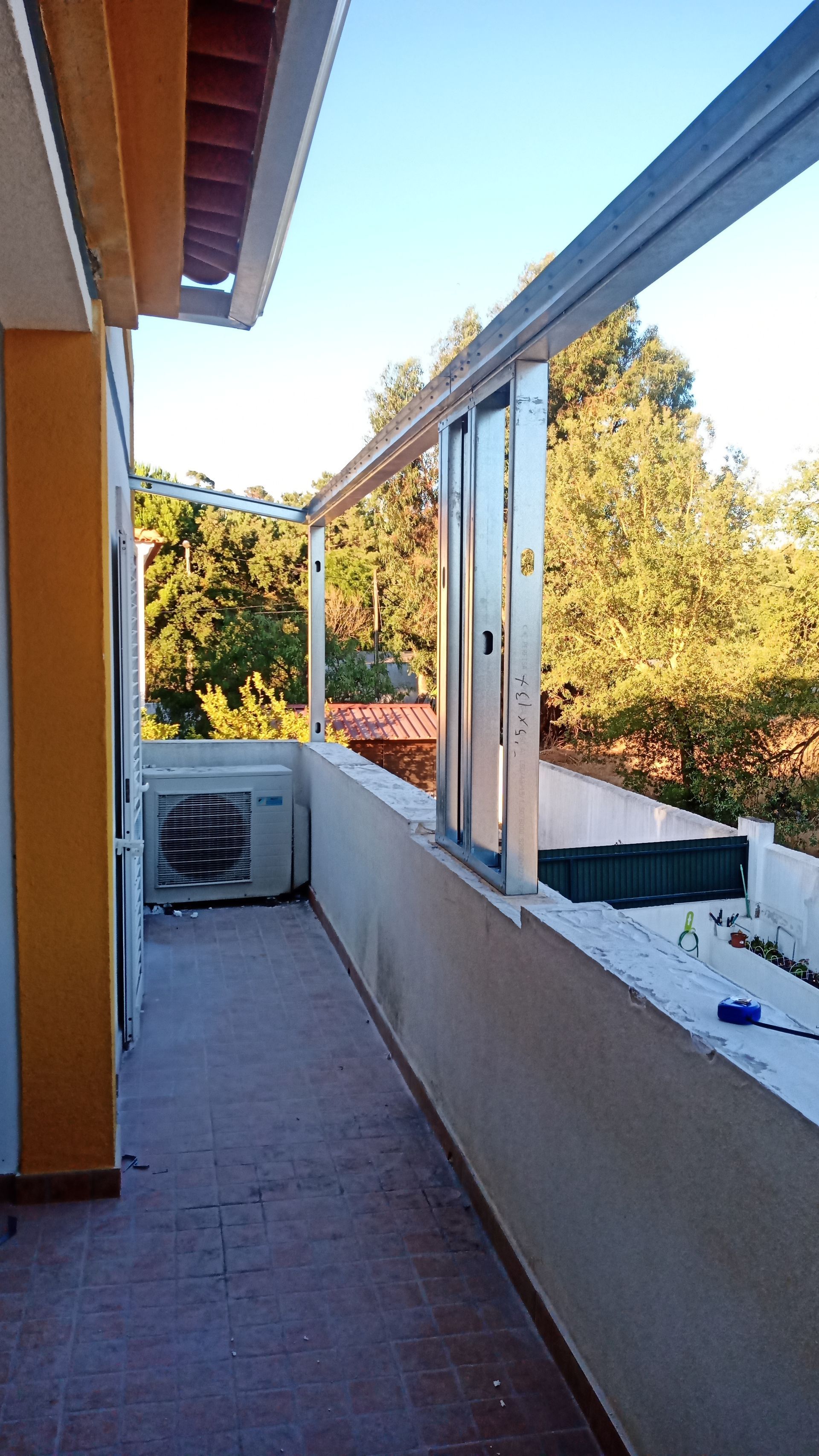 Varanda com ar condicionado, porta de correr de vidro e vista para as árvores.