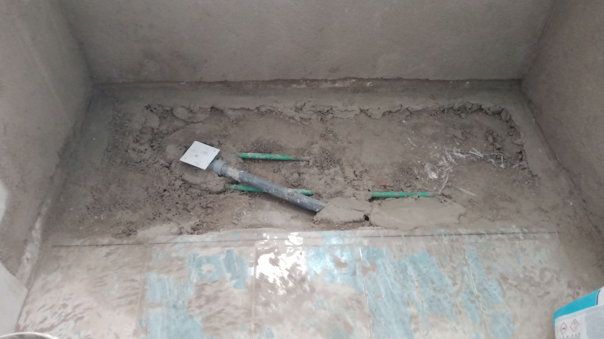 Obra em andamento: base de chuveiro de cimento com encanamento, paredes inacabadas.