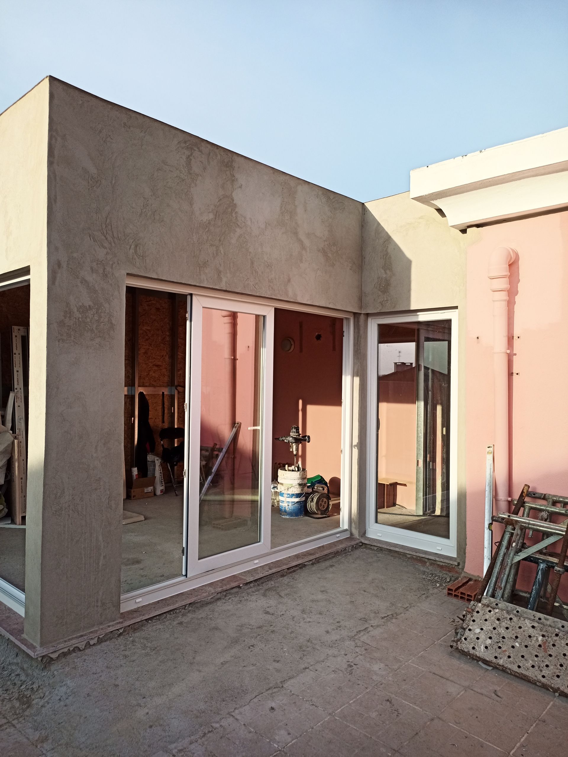 Vista exterior de um edifício em construção. É possível ver portas de vidro deslizantes e paredes cor-de-rosa.
