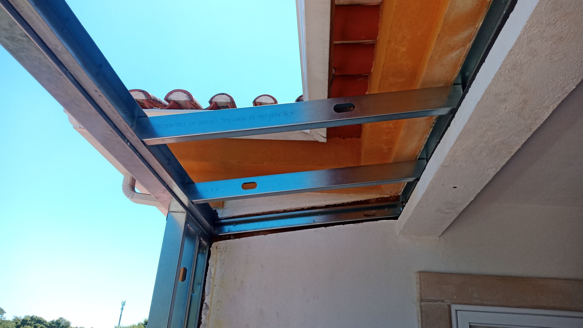 Vigas metálicas que sustentam o telhado na parte externa de um edifício, visíveis contra um céu azul.