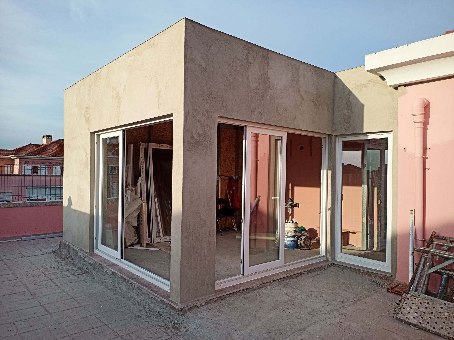 Ampliação do edifício com fachada de concreto inacabado e portas de vidro na cobertura.