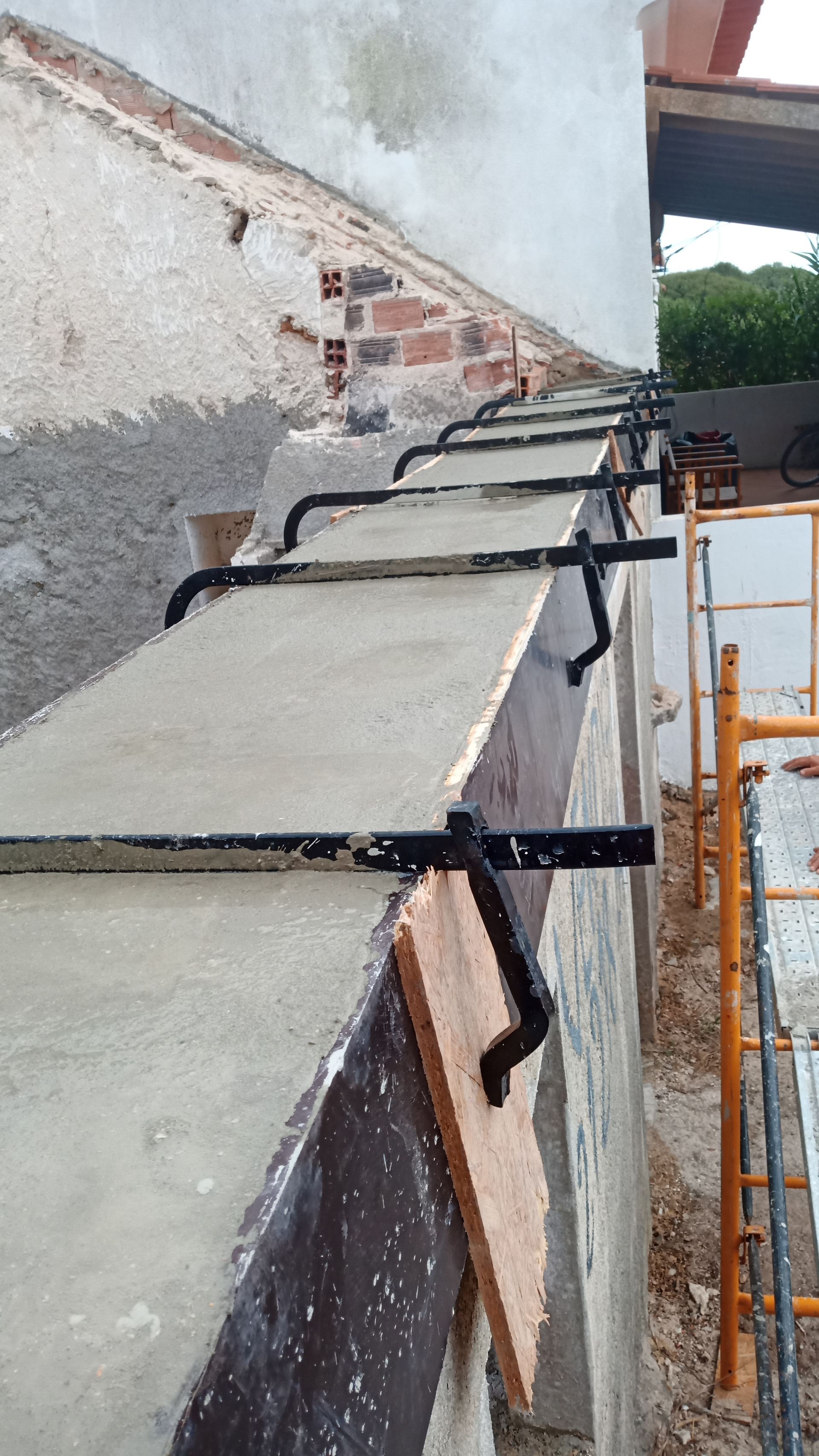 Construção de parede externa com grampos fixando uma laje de concreto. Andaimes visíveis.