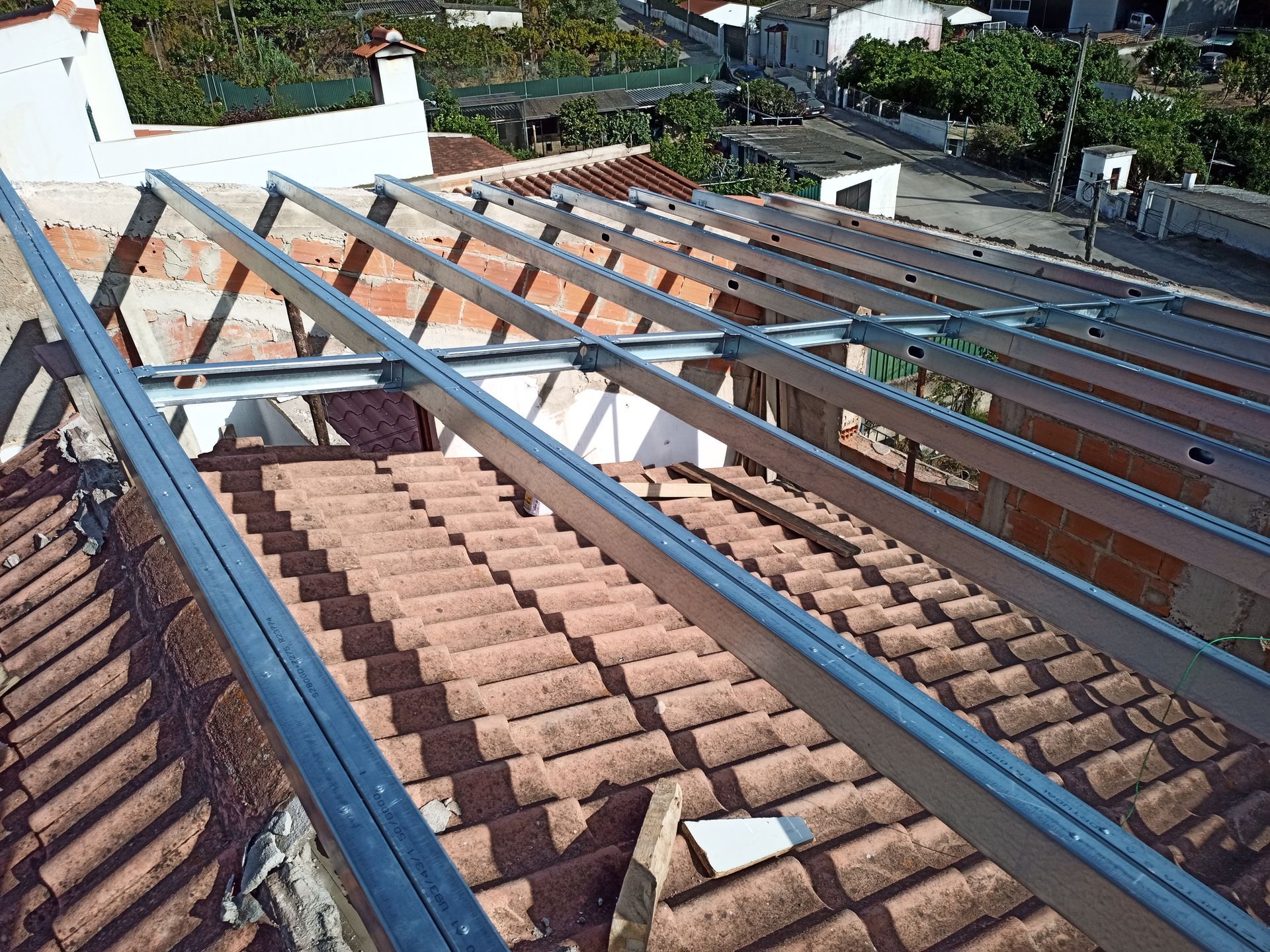Estrutura metálica sendo instalada sobre um telhado de telhas de terracota, com os edifícios circundantes visíveis ao fundo.