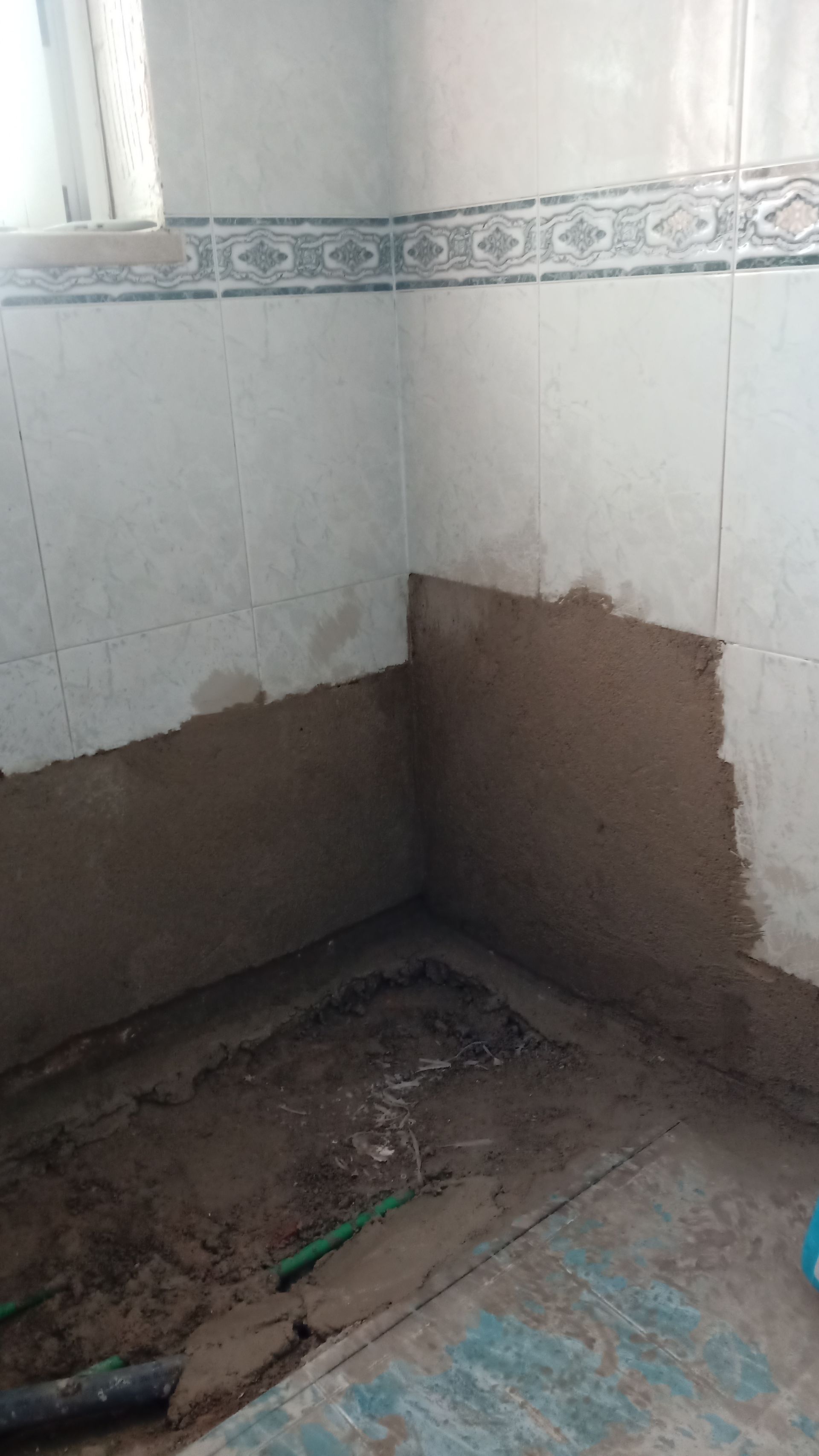 Reforma do banheiro em andamento; paredes com azulejos e gesso fresco, entulho no chão.