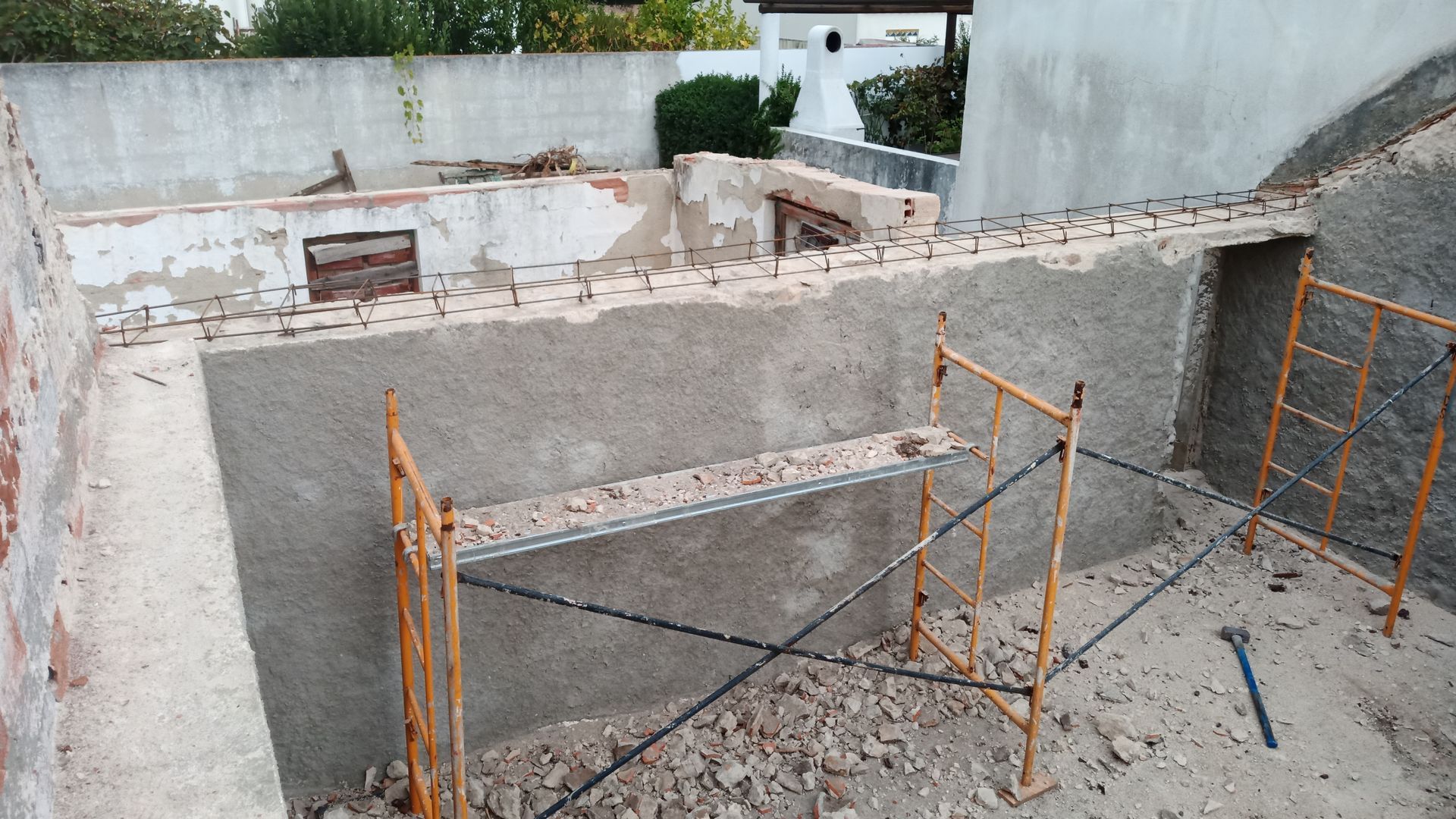 Canteiro de obras: paredes externas, andaimes, concreto, entulho. Paredes parcialmente demolidas, com luz natural.