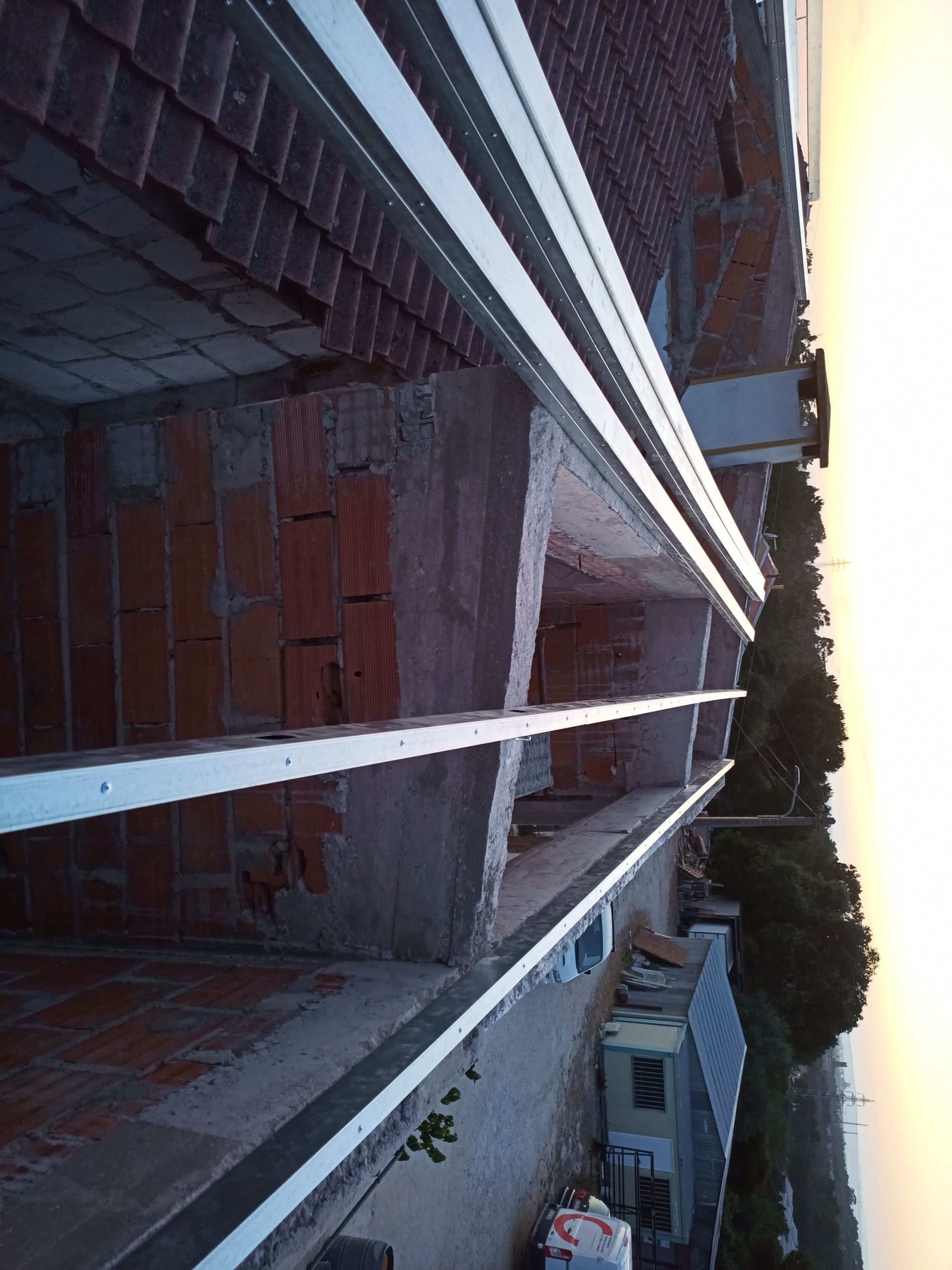 Vista aérea do canteiro de obras com telhado e vigas metálicas brancas.