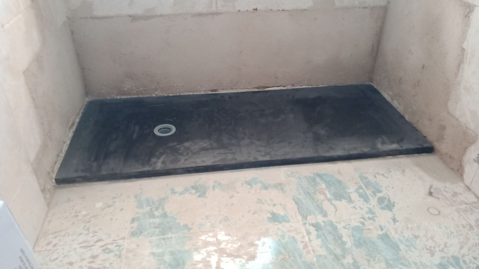 Base de chuveiro retangular preta instalada em um nicho embutido com ralo.