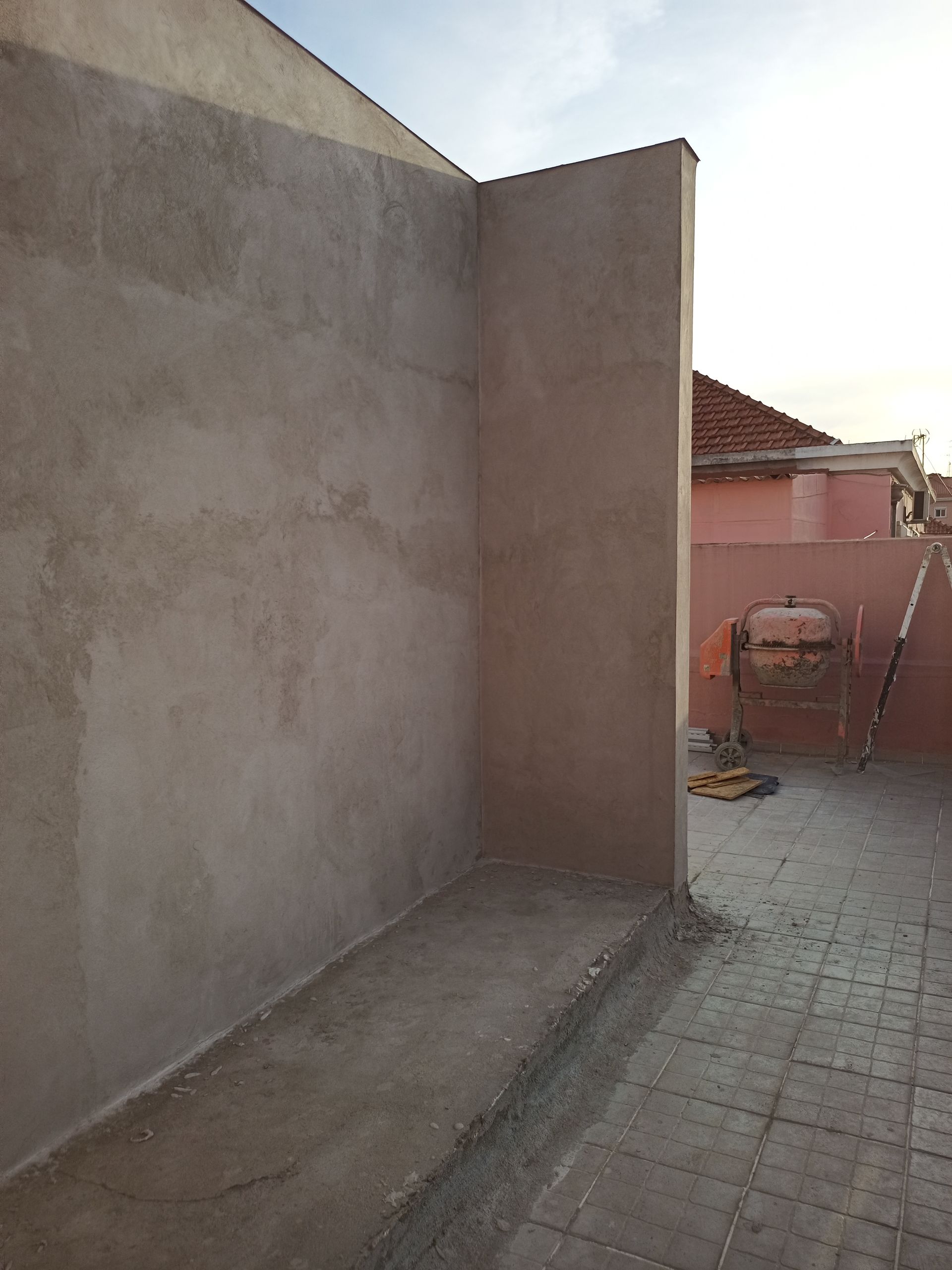 Canto de uma parede de estuque de cor clara em um quintal com um caminho de tijolos.