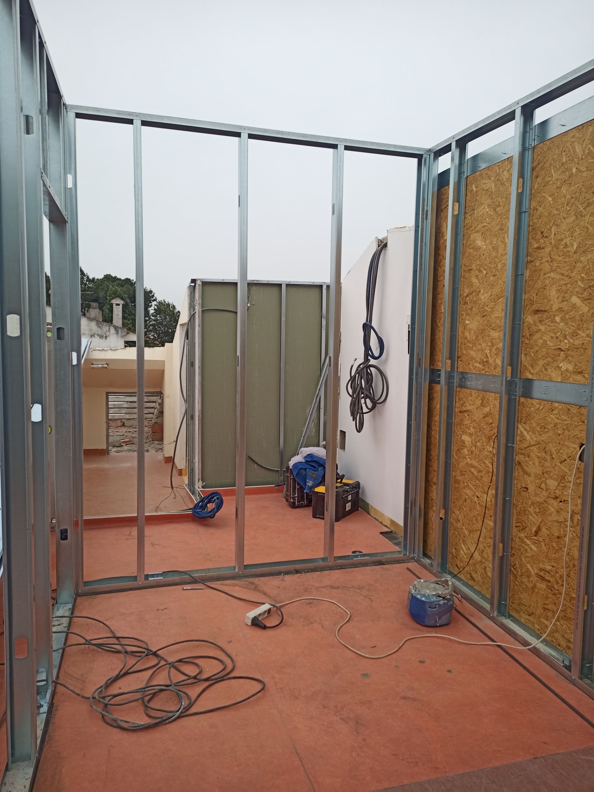 Estrutura metálica das paredes internas de um cômodo em construção; isolamento e painéis de madeira visíveis.