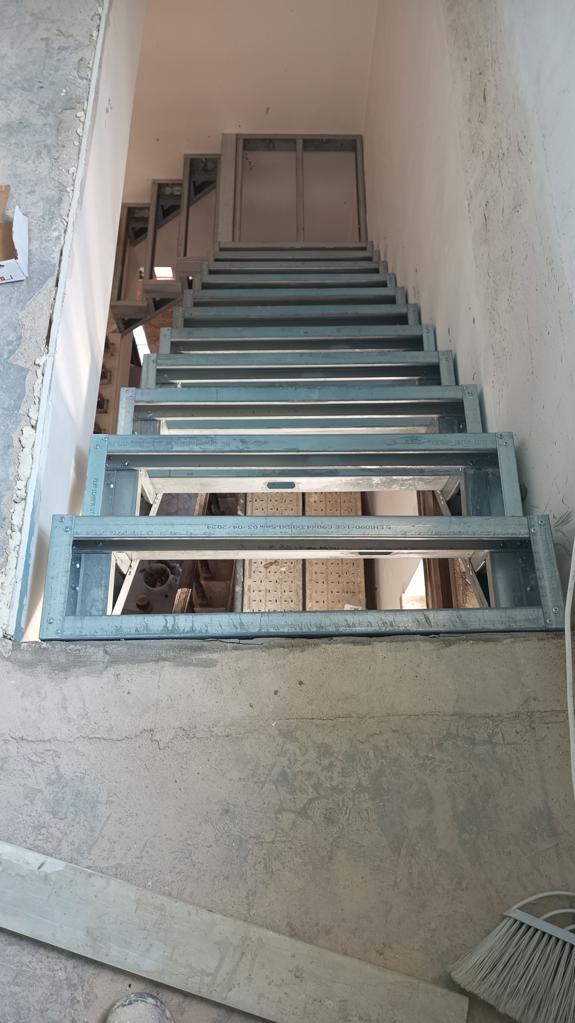 Escada metálica em formato ascendente. Paredes e patamar de concreto.