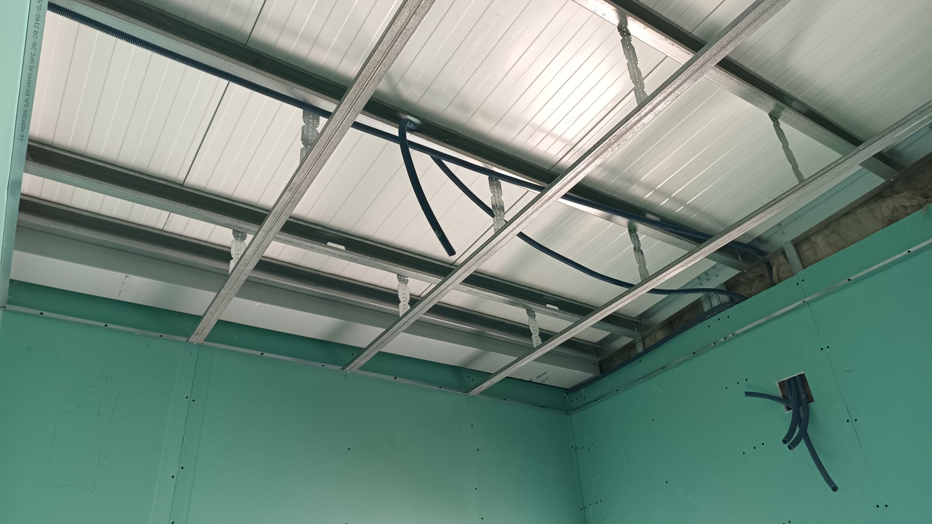 Vista interior mostrando uma estrutura de teto metálica com painéis ondulados e paredes verdes.