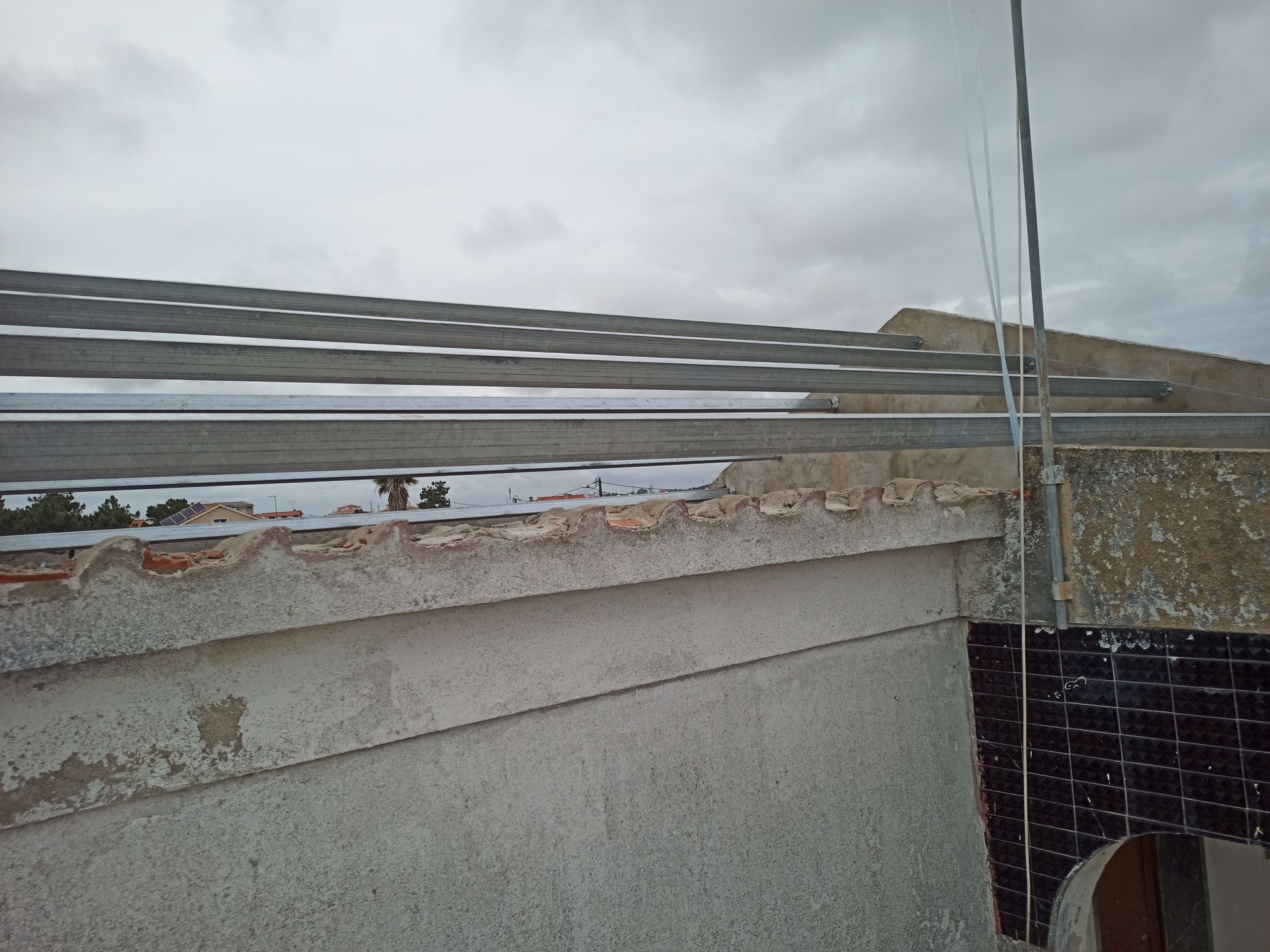 Telhado com vigas de metal e concreto desgastado sob um céu nublado.