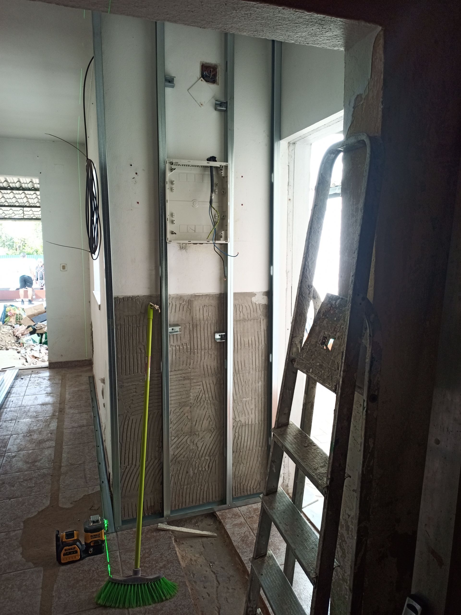 Construção interna em andamento: estrutura metálica, escada, vassoura, paredes parcialmente acabadas e porta.