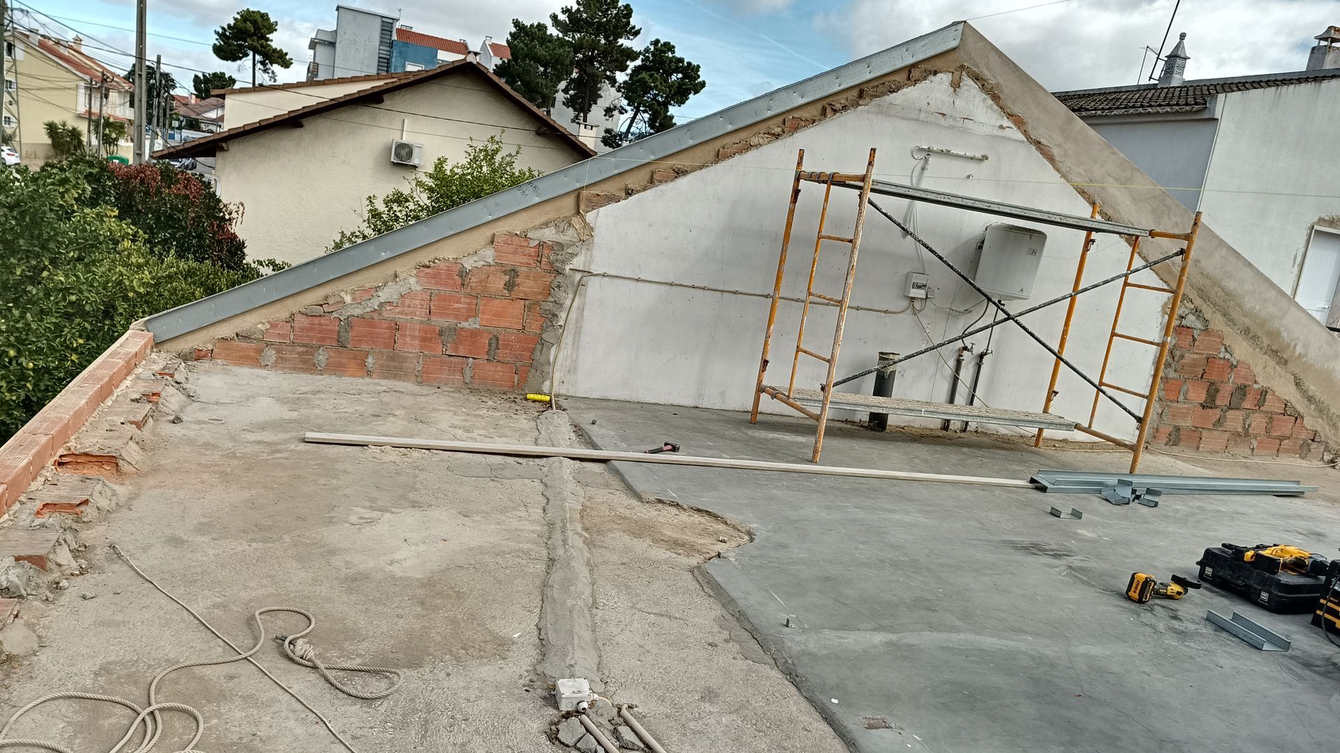 Canteiro de obras em um telhado, com tijolos aparentes, andaimes e parede parcialmente demolida.