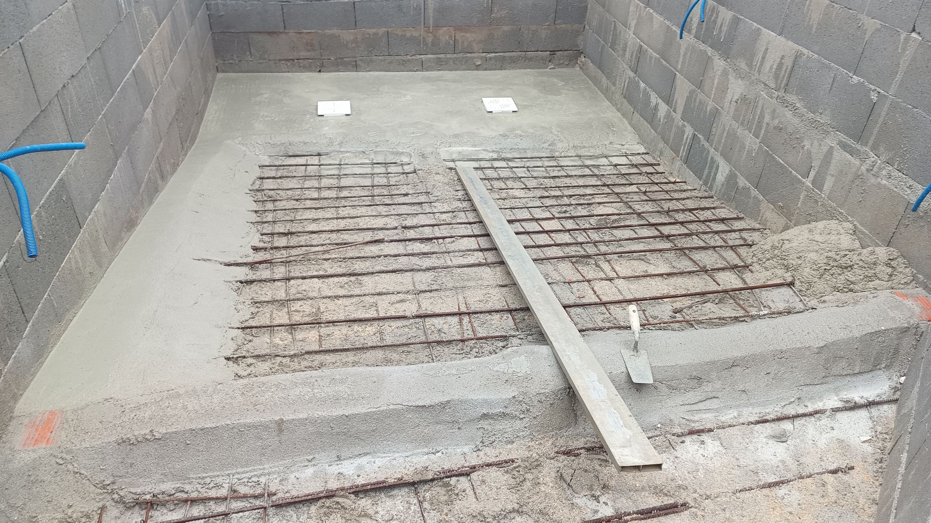 Piso de concreto sendo assentado em uma estrutura retangular de alvenaria com reforço de vergalhão.