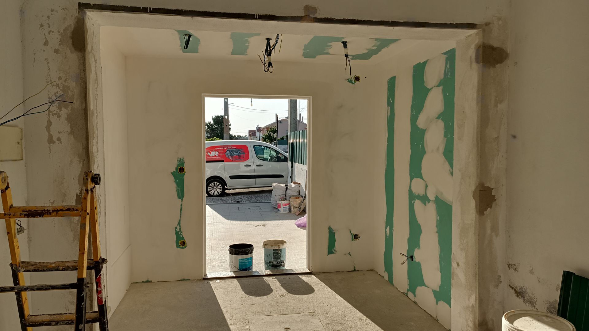 Reforma em andamento: porta de entrada com paredes remendadas de verde, escada e uma van estacionada do lado de fora.