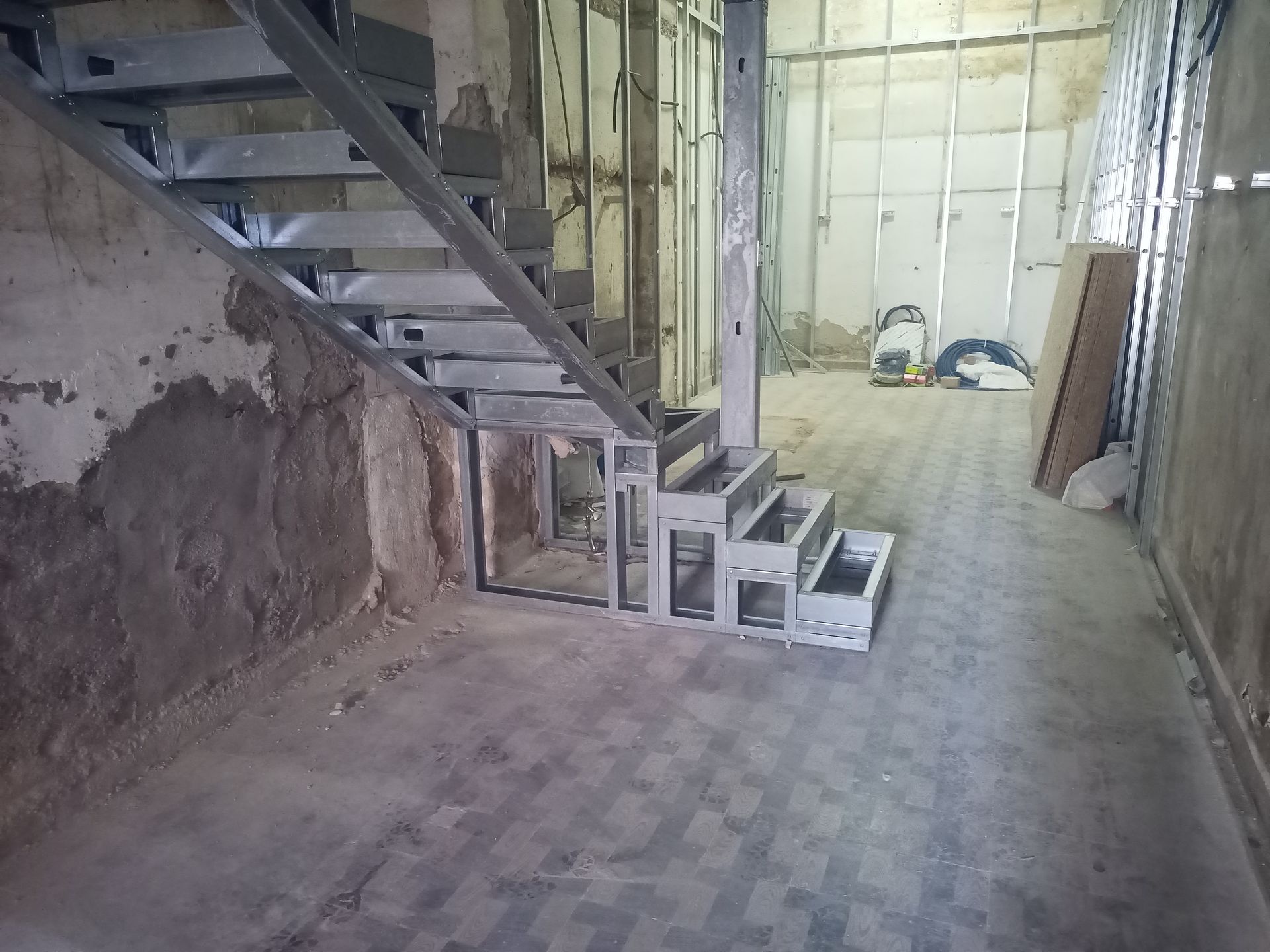 Escada metálica em construção em um cômodo, com vigas expostas e paredes inacabadas.