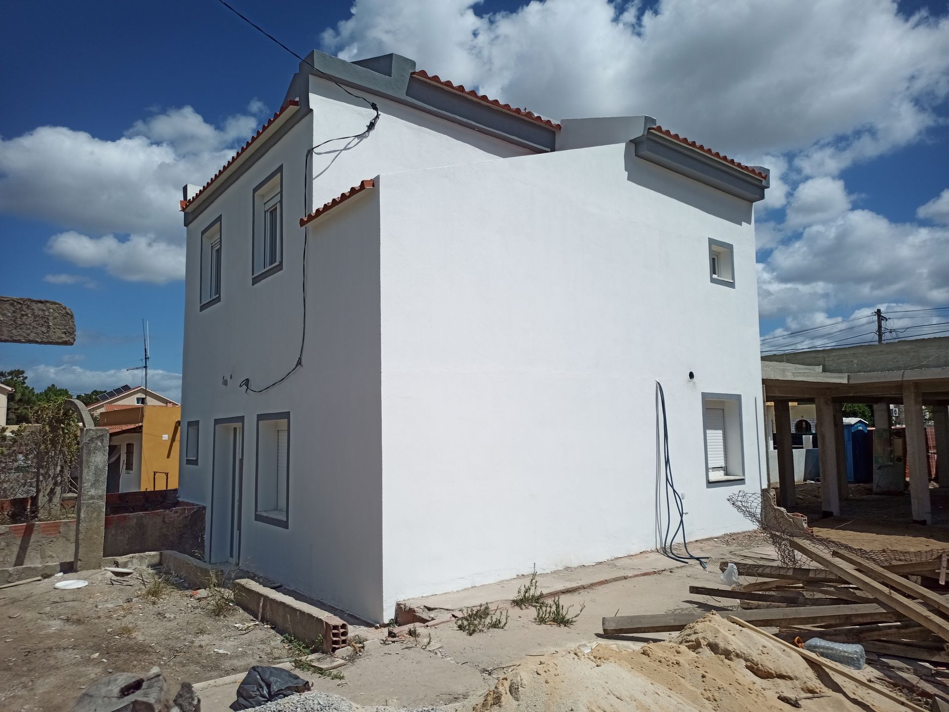 Prédio branco de dois andares em construção, com telhado cinza e céu azul.