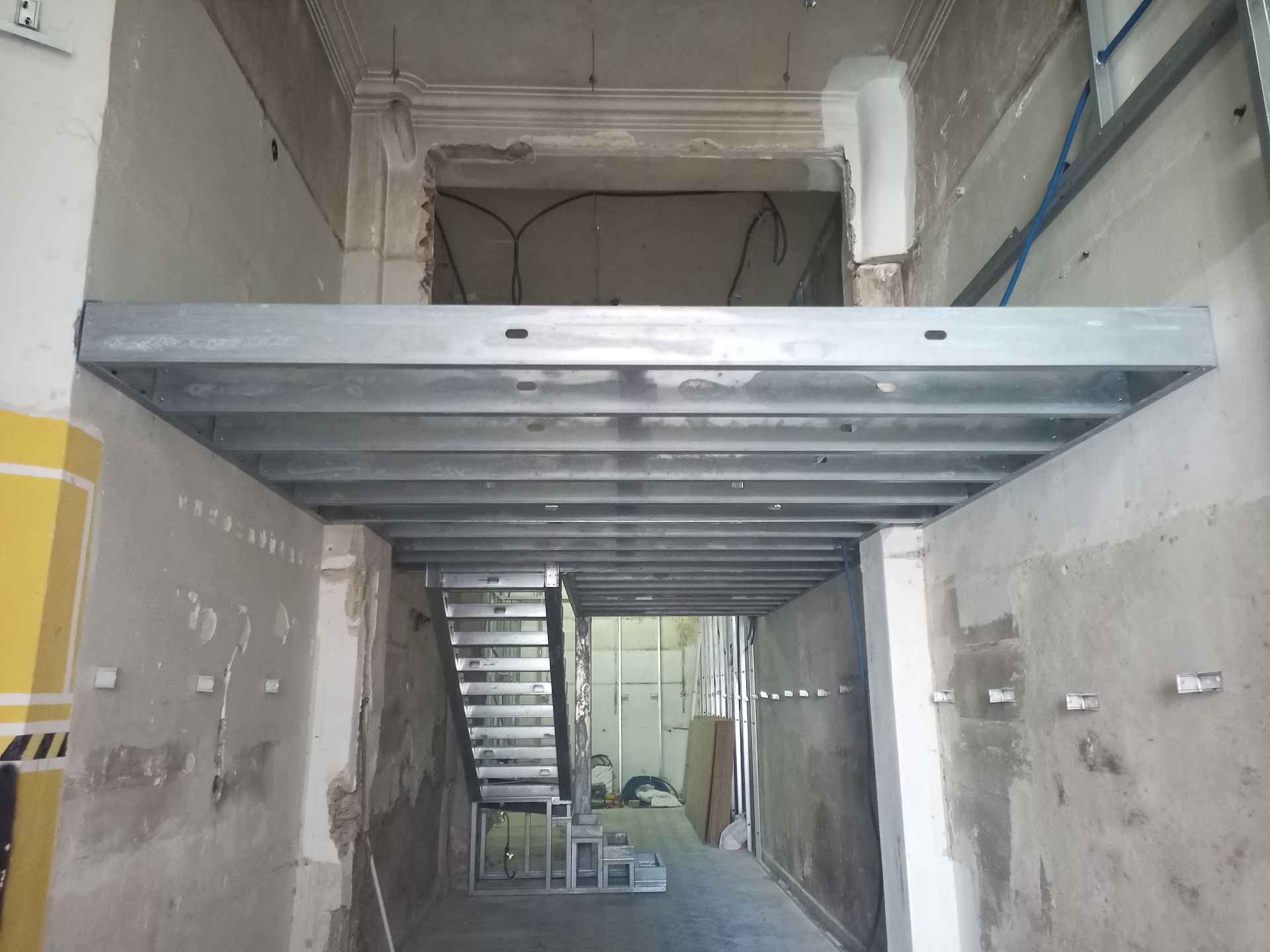 Estrutura metálica de um mezanino em construção. Escada de acesso ao mezanino, vista do corredor.