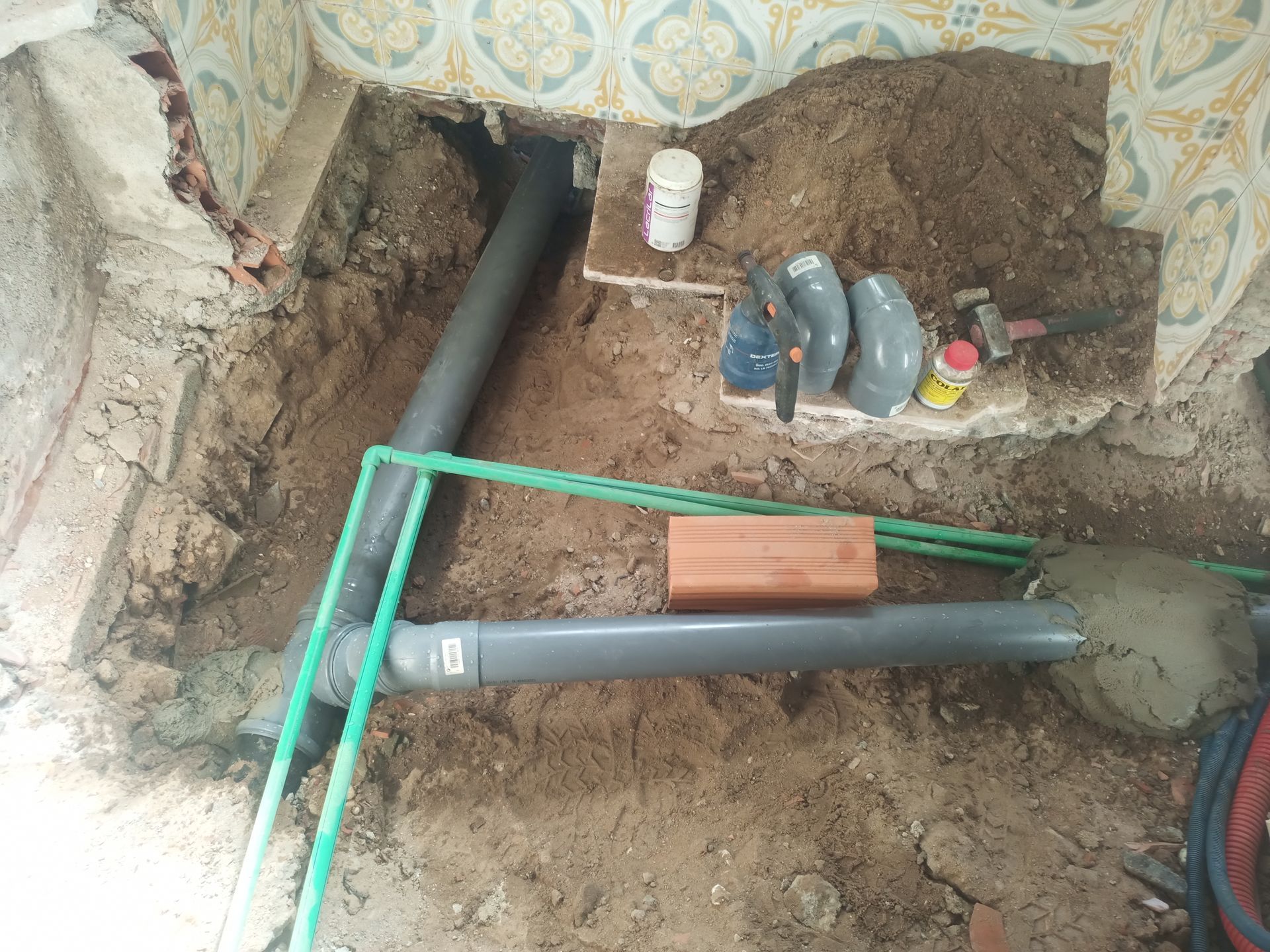 Reparo hidráulico em andamento: canos, conexões, sujeira e ferramentas dentro de um cômodo com azulejos.