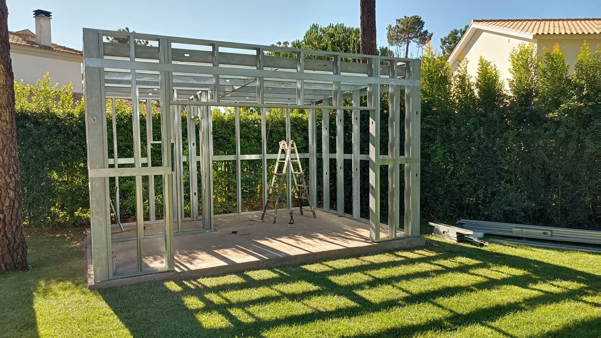 Estrutura metálica de um pequeno edifício em construção, sobre grama verde, em um dia ensolarado.