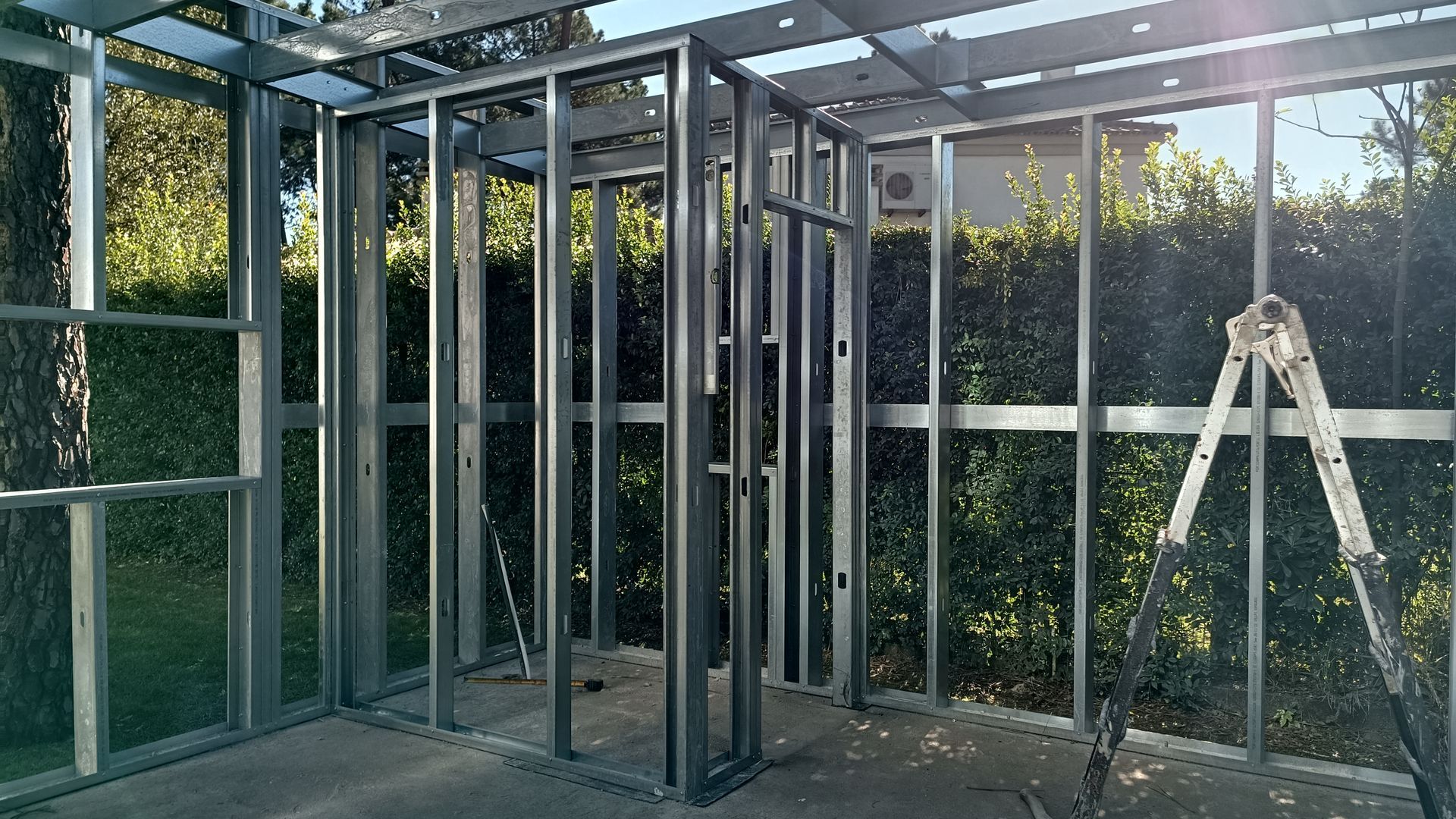 Estrutura metálica de uma construção em andamento; paredes e uma porta são visíveis.