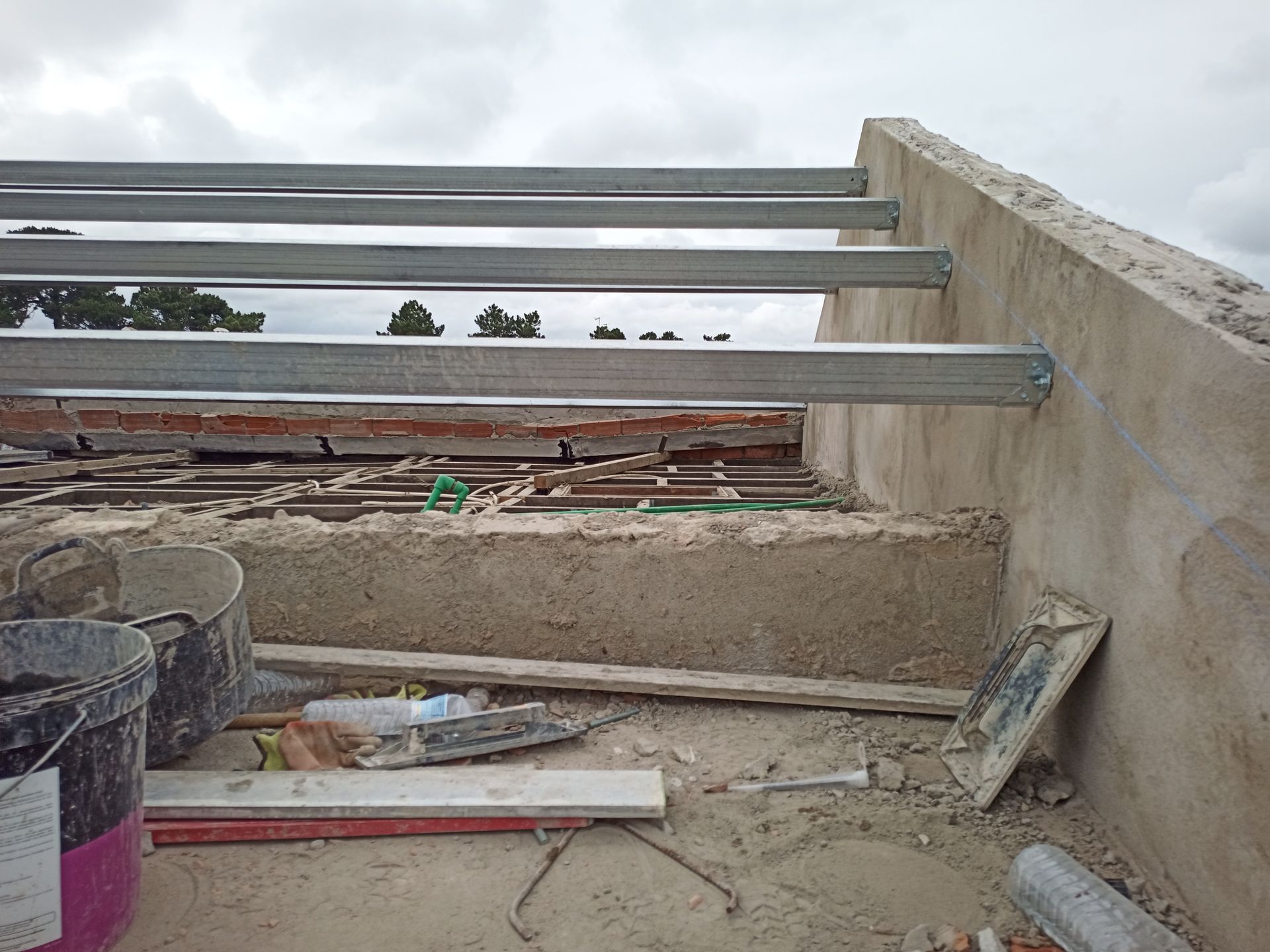 Canteiro de obras com vigas metálicas e estrutura de concreto; telhado inacabado.