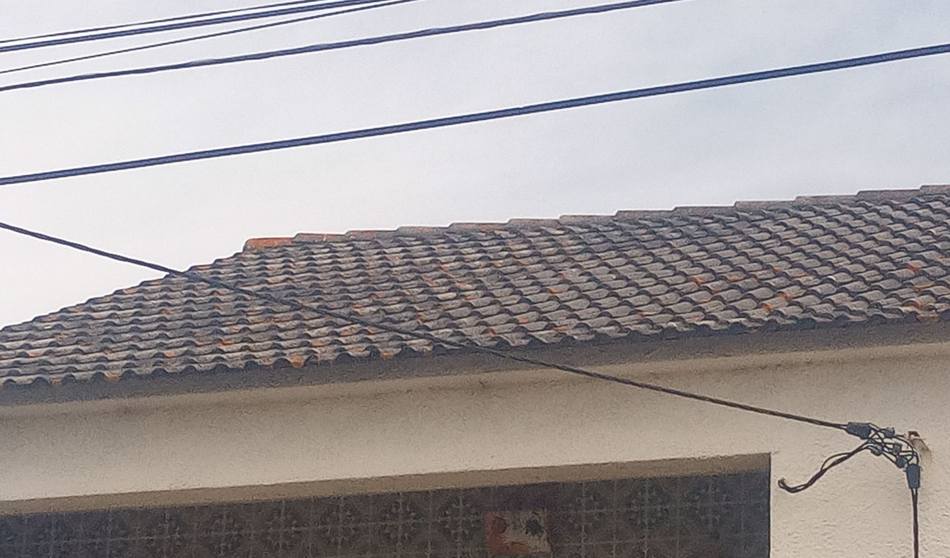 Telhado com telhas e fiação elétrica aparente.