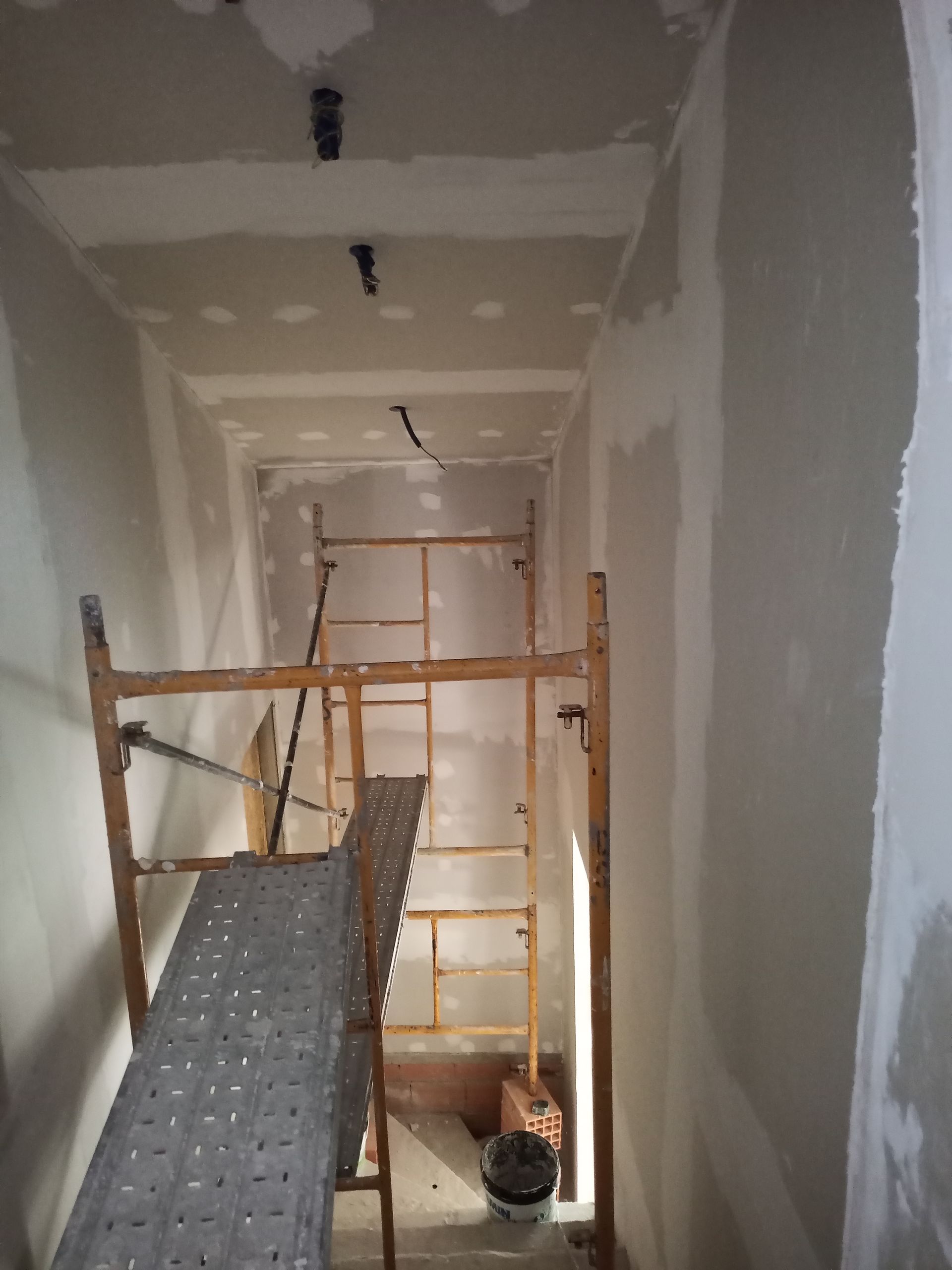 Corredor em construção com andaimes e drywall.