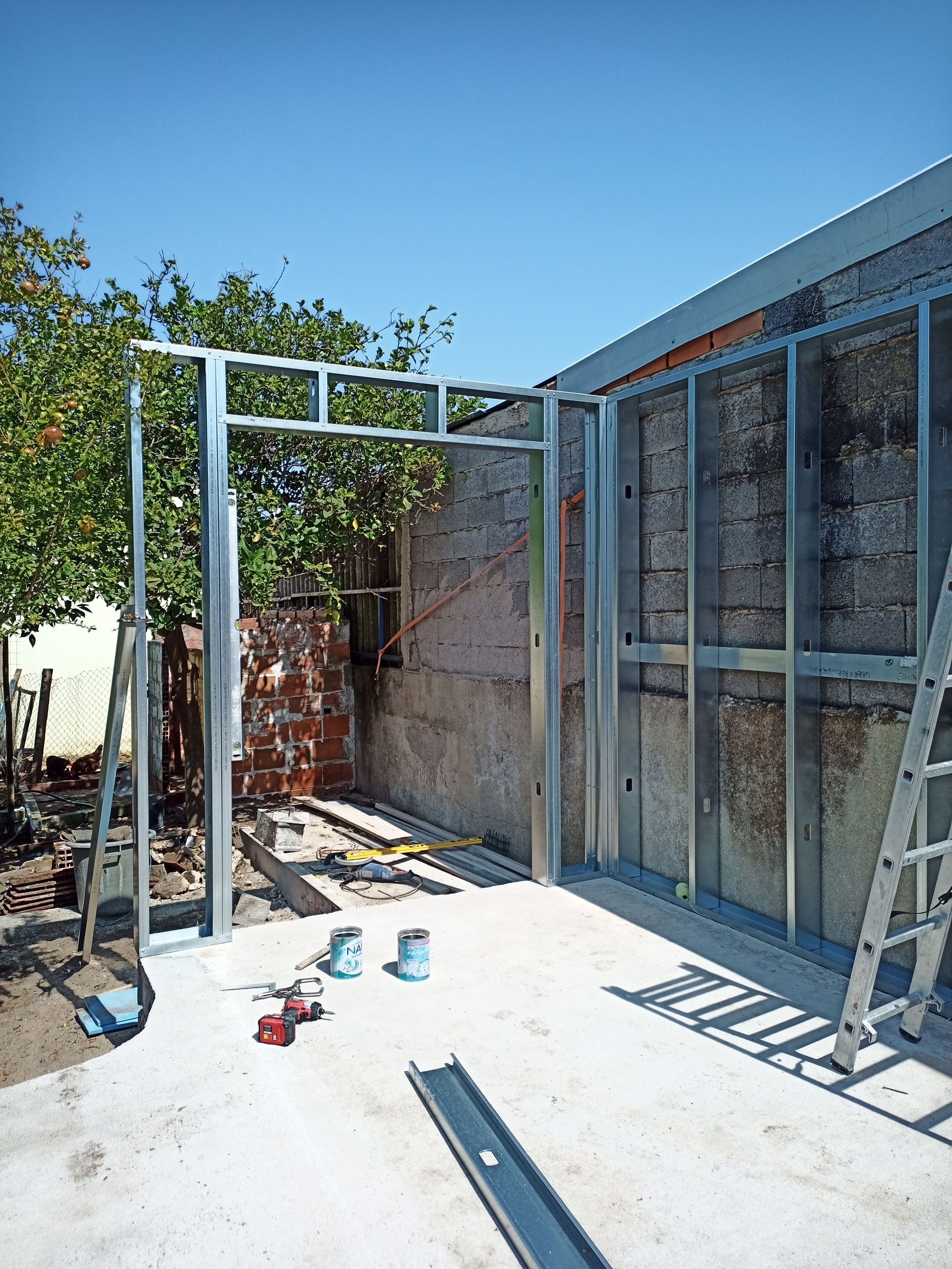 Estrutura metálica interna de um edifício, encostada em uma parede de tijolos, sob um céu claro.