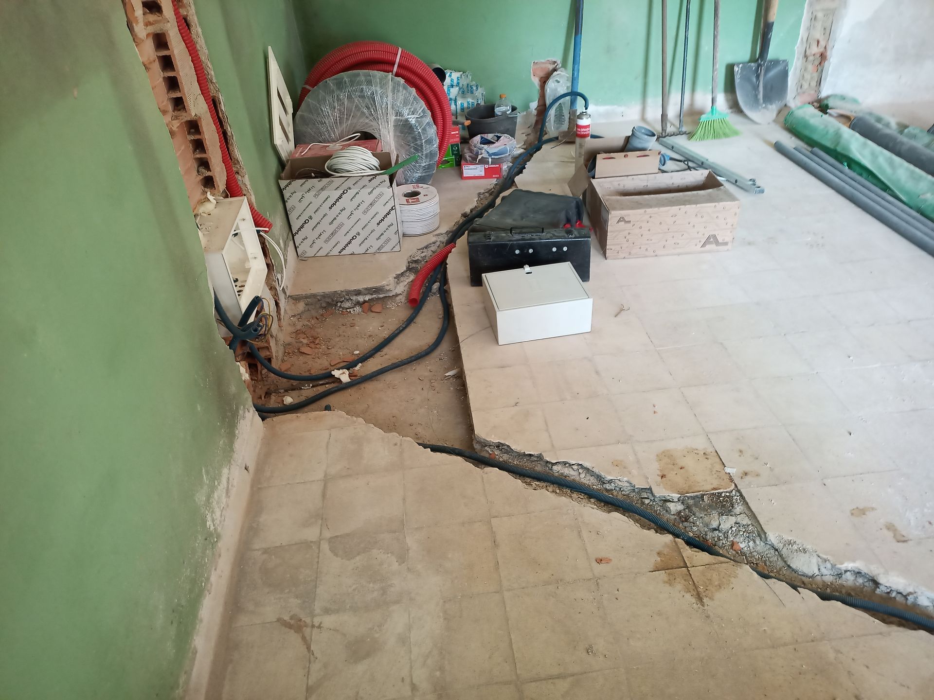 Cômodo em construção, com fiação e encanamento expostos. Diversas ferramentas e materiais espalhados pelo chão.